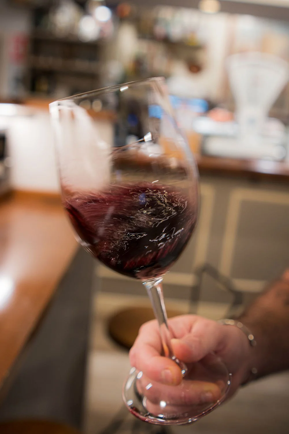 Vaso de vino tinto en una mano, con fondo difuso de una barra o una cocina.