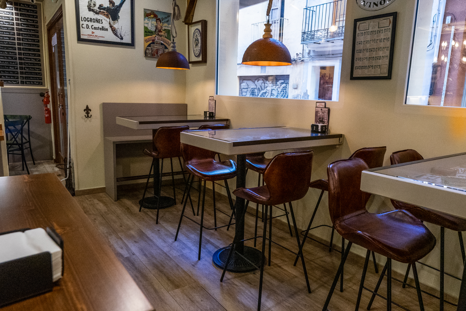 Interior de un restaurante con mesas y sillas de cuero, luz cálida y paredes decoradas con carteles y fotografías vintage.