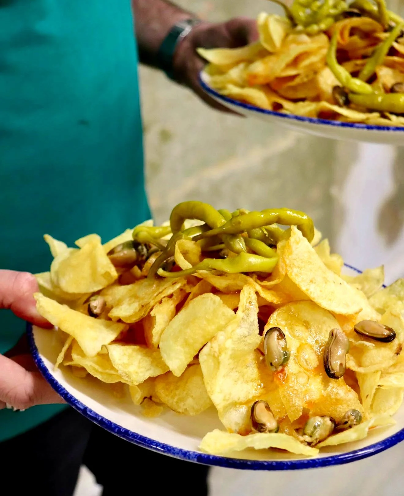 Una persona sostiene un plato de patatas fritas "papas" cubiertos con mejillones en escabeche y piparras.
