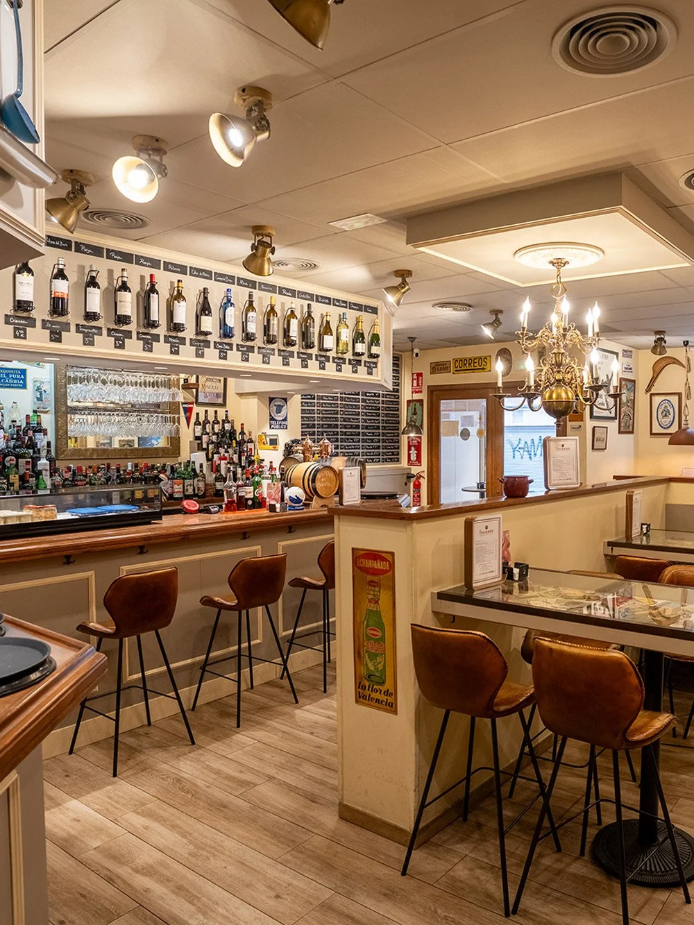Bar con sillas de cuero, estantería con botellas de vino y licor, lámparas de techo, candelabro, y decoraciones clásicas en un restaurante.
