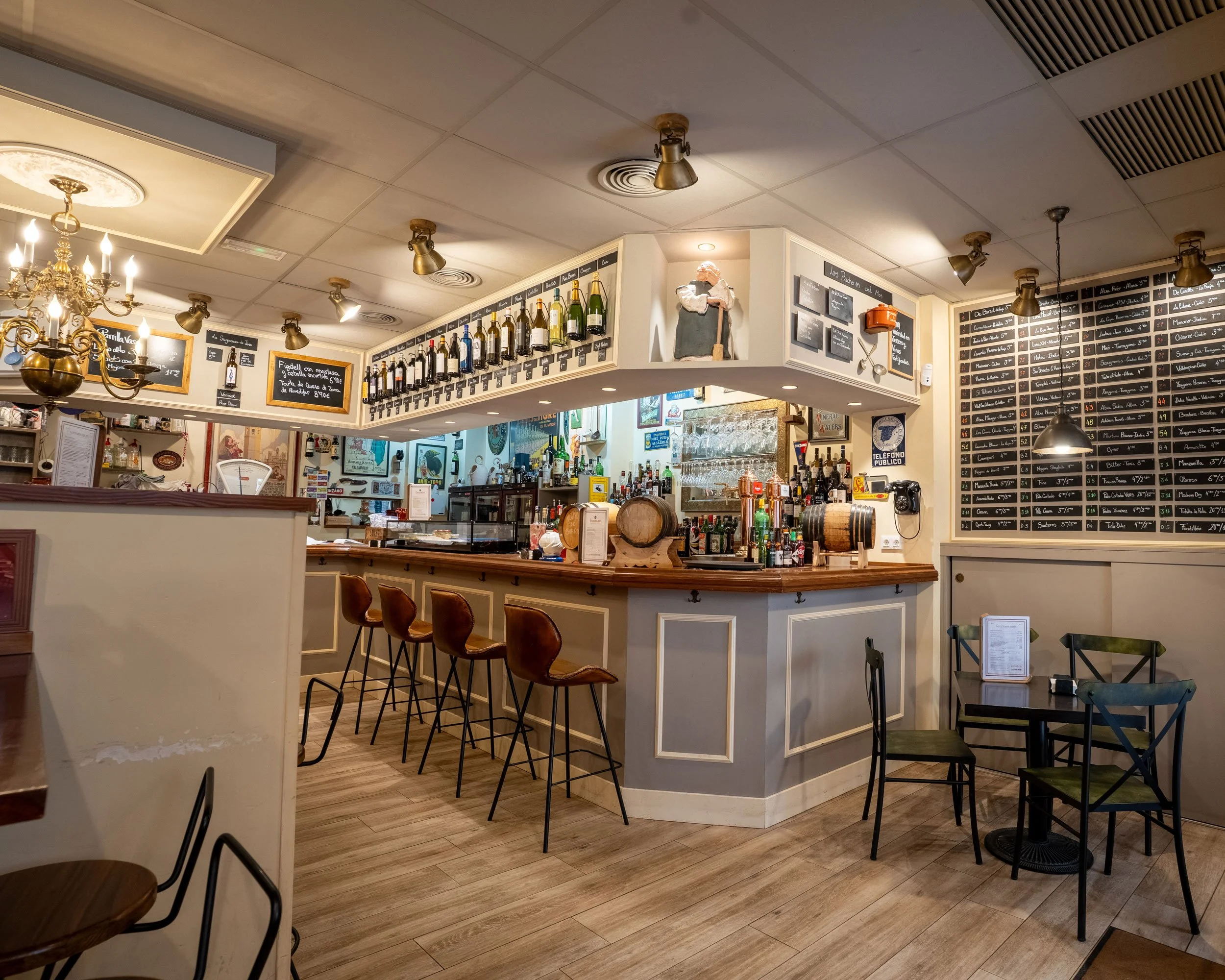 Bar de restaurante con barras de madera, estanterías con botellas y mesas con sillas, en un interior cálido y bien iluminado.