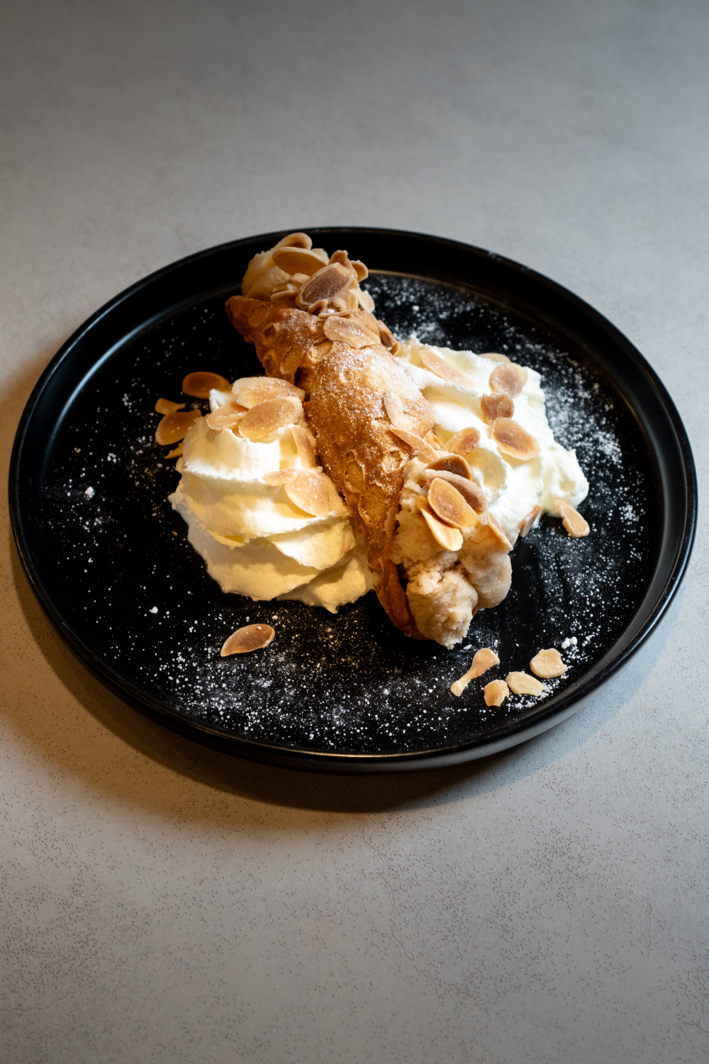 Postre con helado de vainilla, un dulce de churro y almendras en una bandeja negra