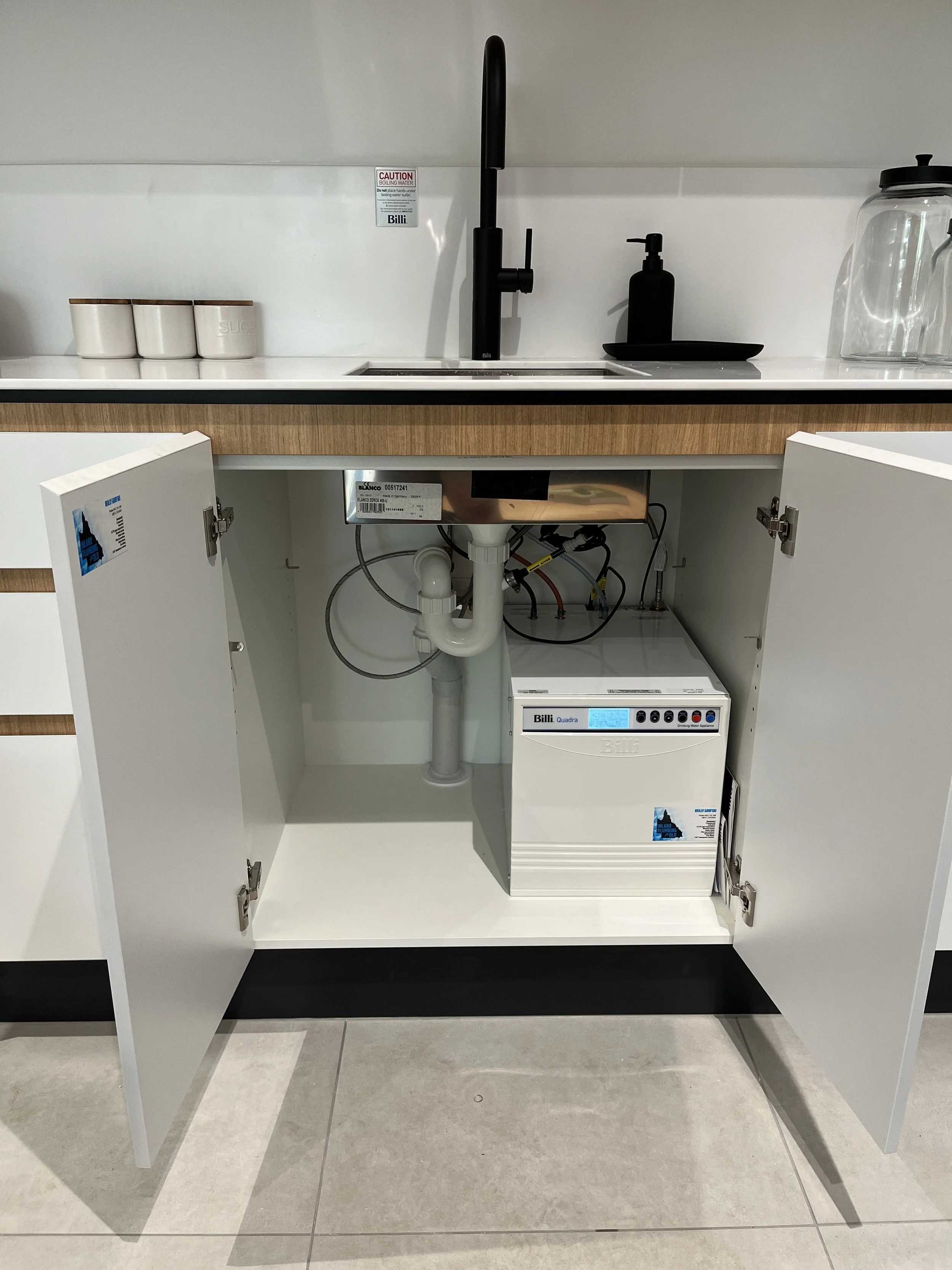 Open kitchen cabinet under a laboratory sink showing plumbing and a water filtration system.