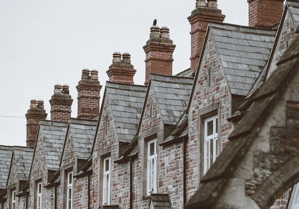 Row of old brick row houses with chimneys, pitched roofs, and small windows, under an overcast sky.