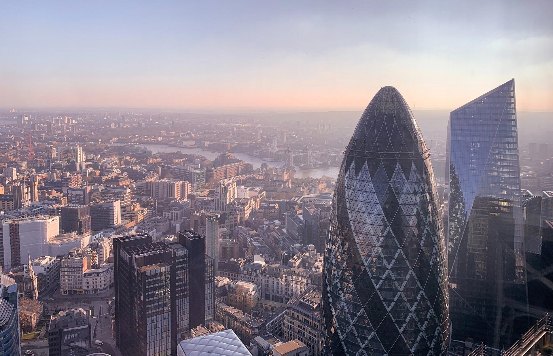 Aerial view of London skyline with modern skyscrapers, including the Gherkin and the Leadenhall Building, during sunset.