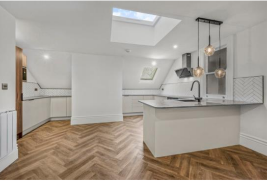 Modern kitchen with white cabinets, a central island with a sink, three pendant lights, hardwood flooring, and skylights in the ceiling.