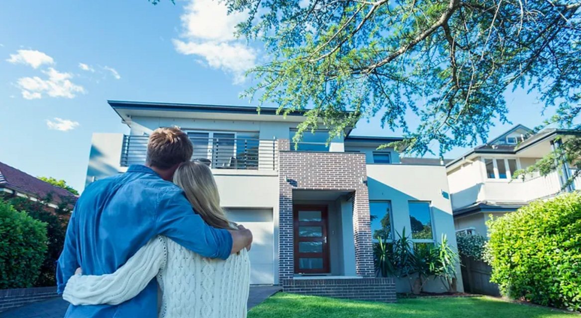 A couple standing outside a modern house, embracing each other on a sunny day with blue sky.