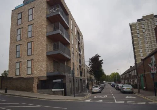 A multi-story residential building on a city street with parked cars and a no-parking sign.