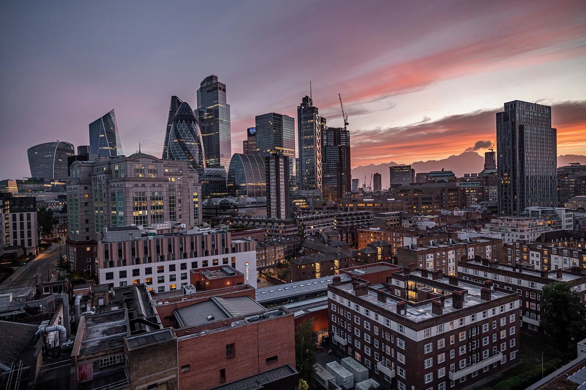 Skyline of London with modern skyscrapers at sunset, featuring the Gherkin building and other contemporary high-rises.