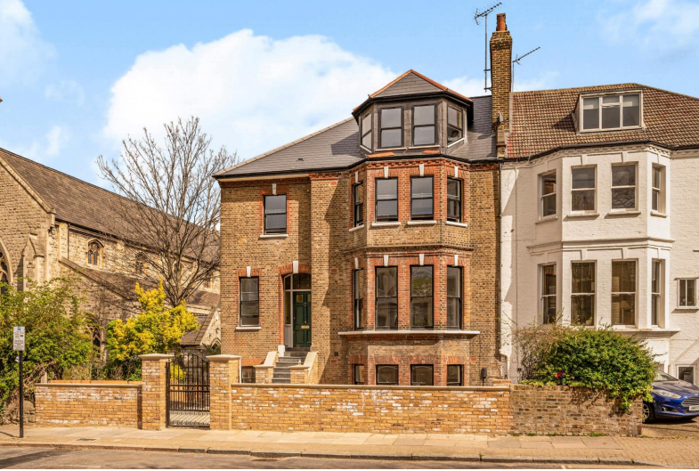 A large brick house with bay windows and a small front yard enclosed by a brick wall.
