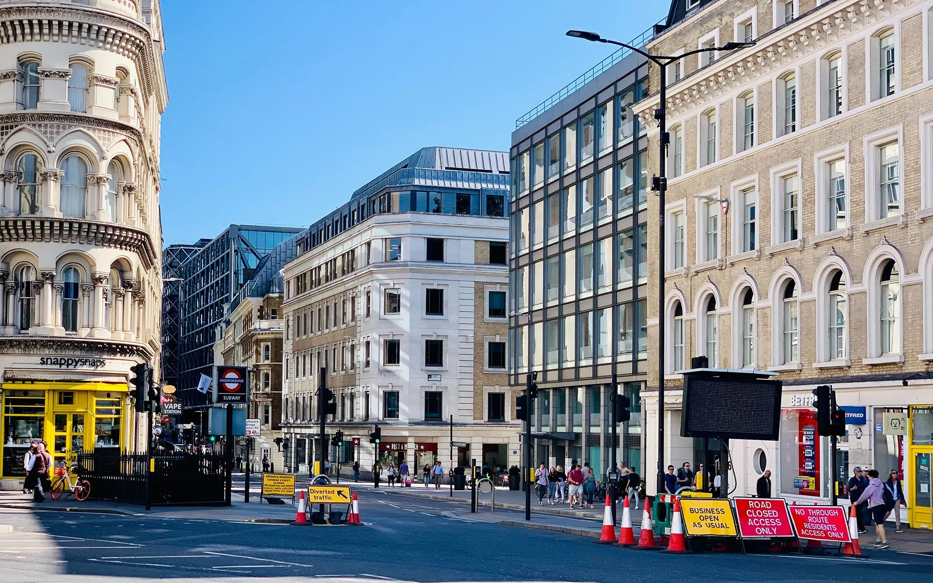 Street scene in London with people walking, traffic signs, and modern buildings under a blue sky.