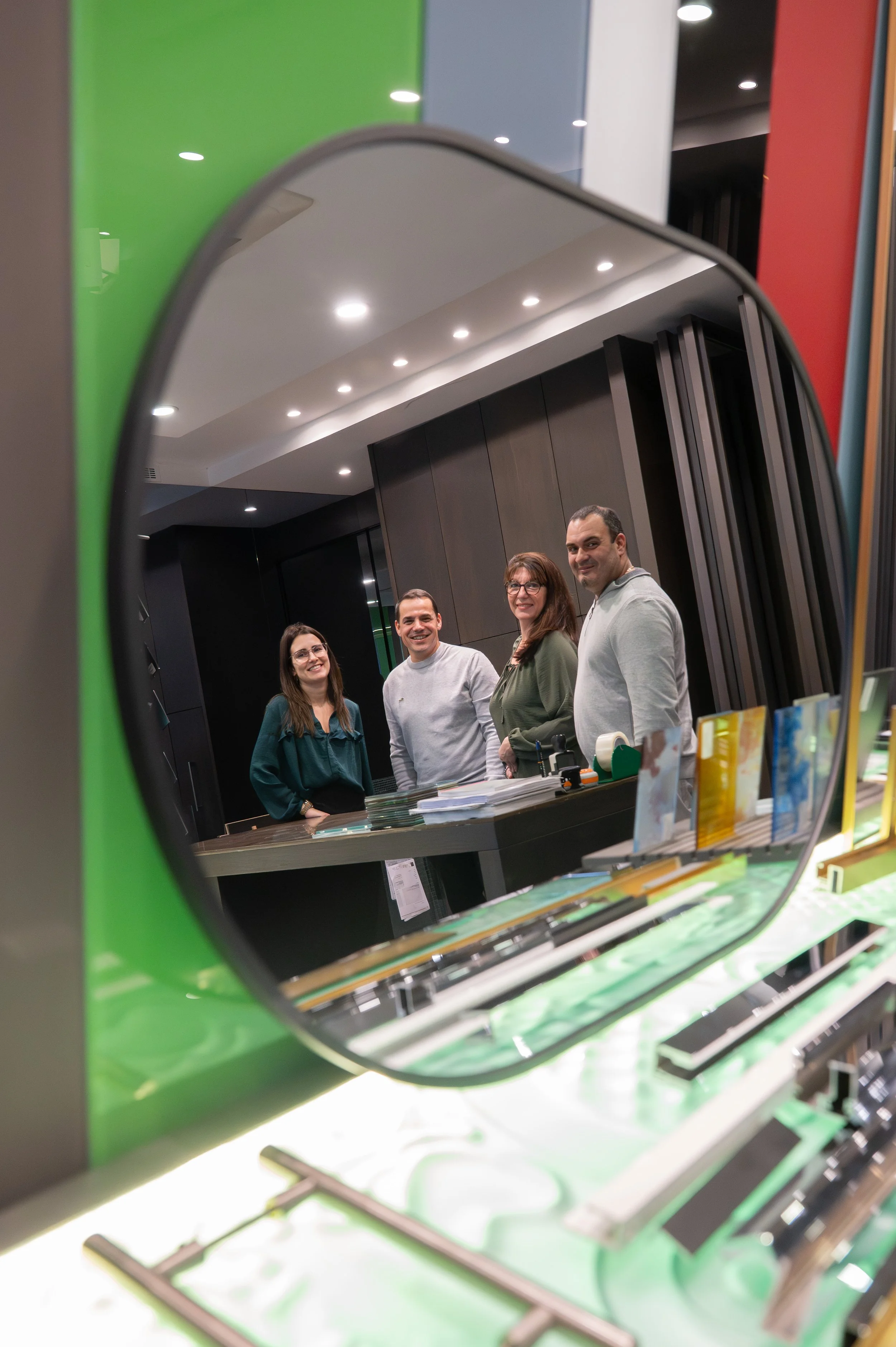 Reflet d'un groupe de quatre personnes souriantes dans un miroir dans un espace intérieur moderne.