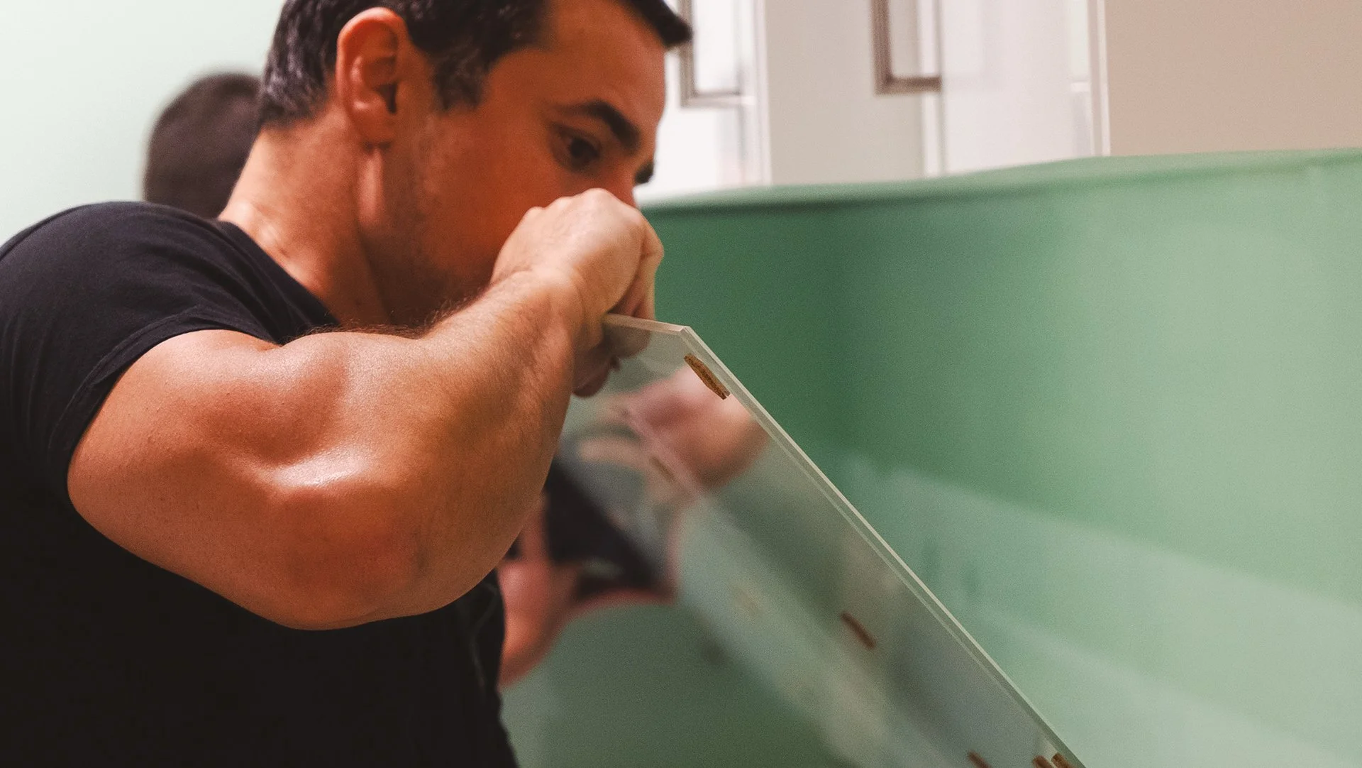 Un homme s'appuie sur un panneau en verre ou en plastique dans un environnement intérieur.
