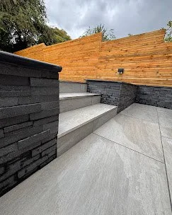 Outdoor staircase with concrete steps, black brick walls, and a wooden privacy fence in the background.