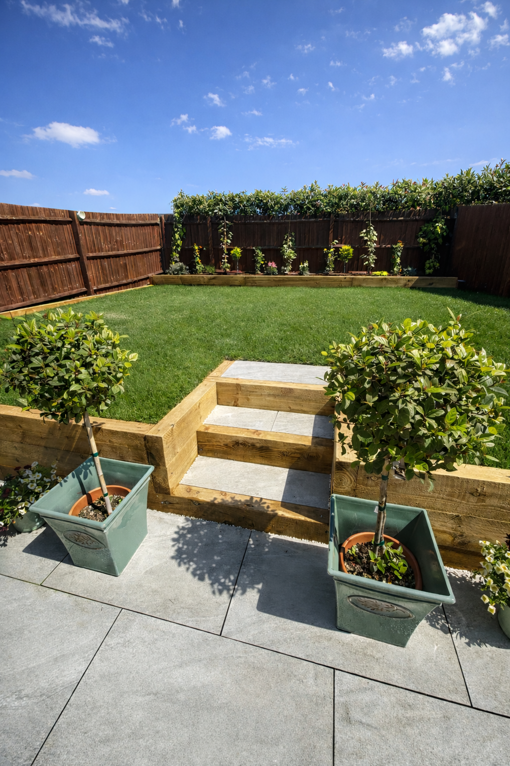 Landscaped garden with porcelain patio, sleeper retaining walls and steps, turf and planting