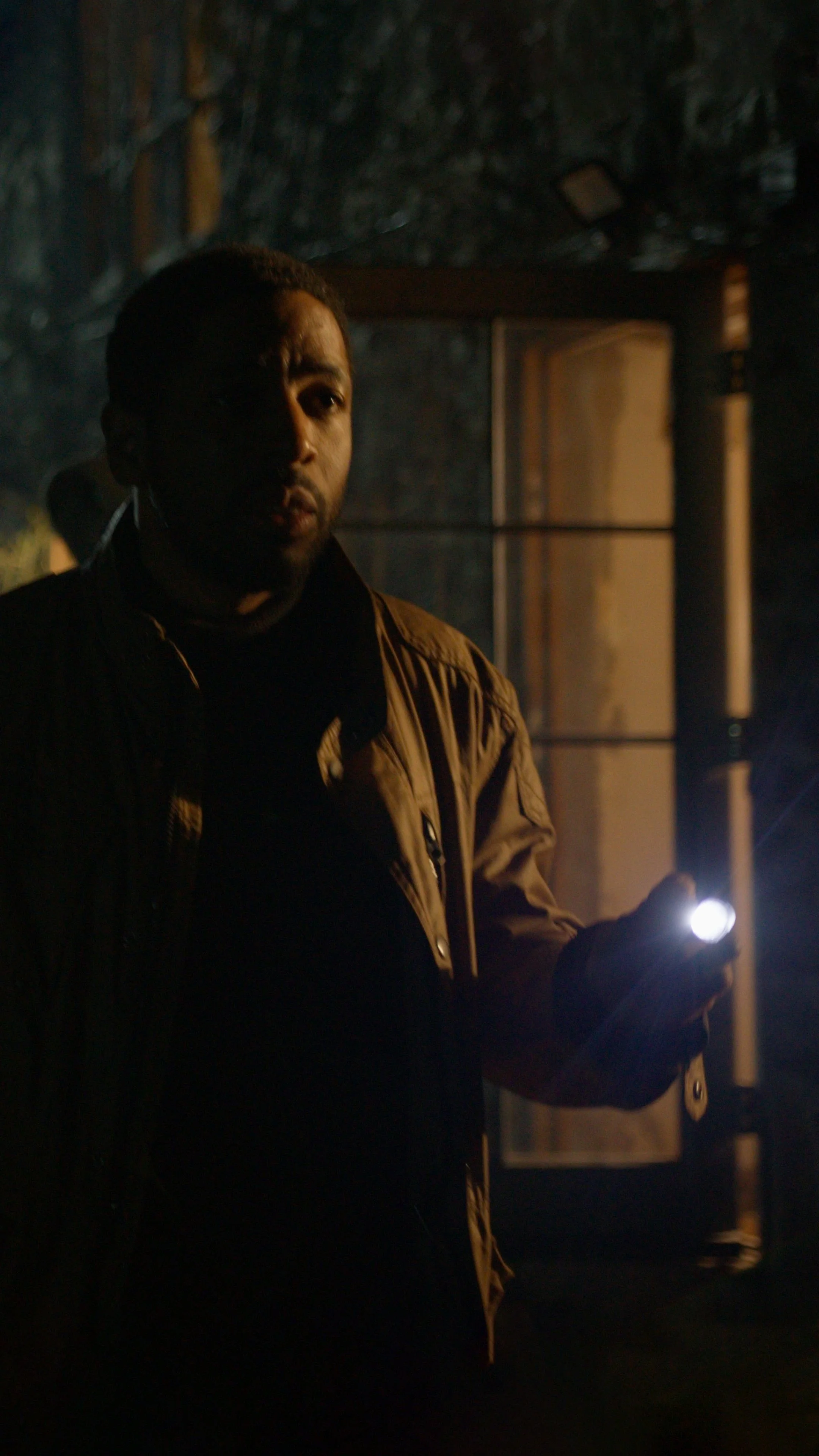 A man holding a flashlight in a dark room with a speaker in the background.