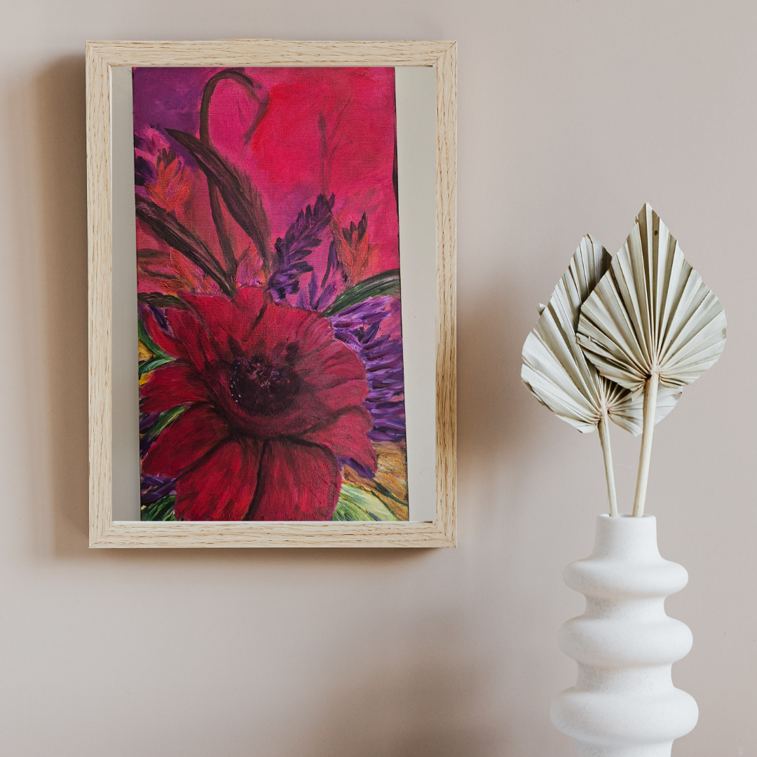 A framed, colourful floral painting displayed on a neutral wall beside simple natural objects, highlighting the artwork’s expressive colour and balanced composition.