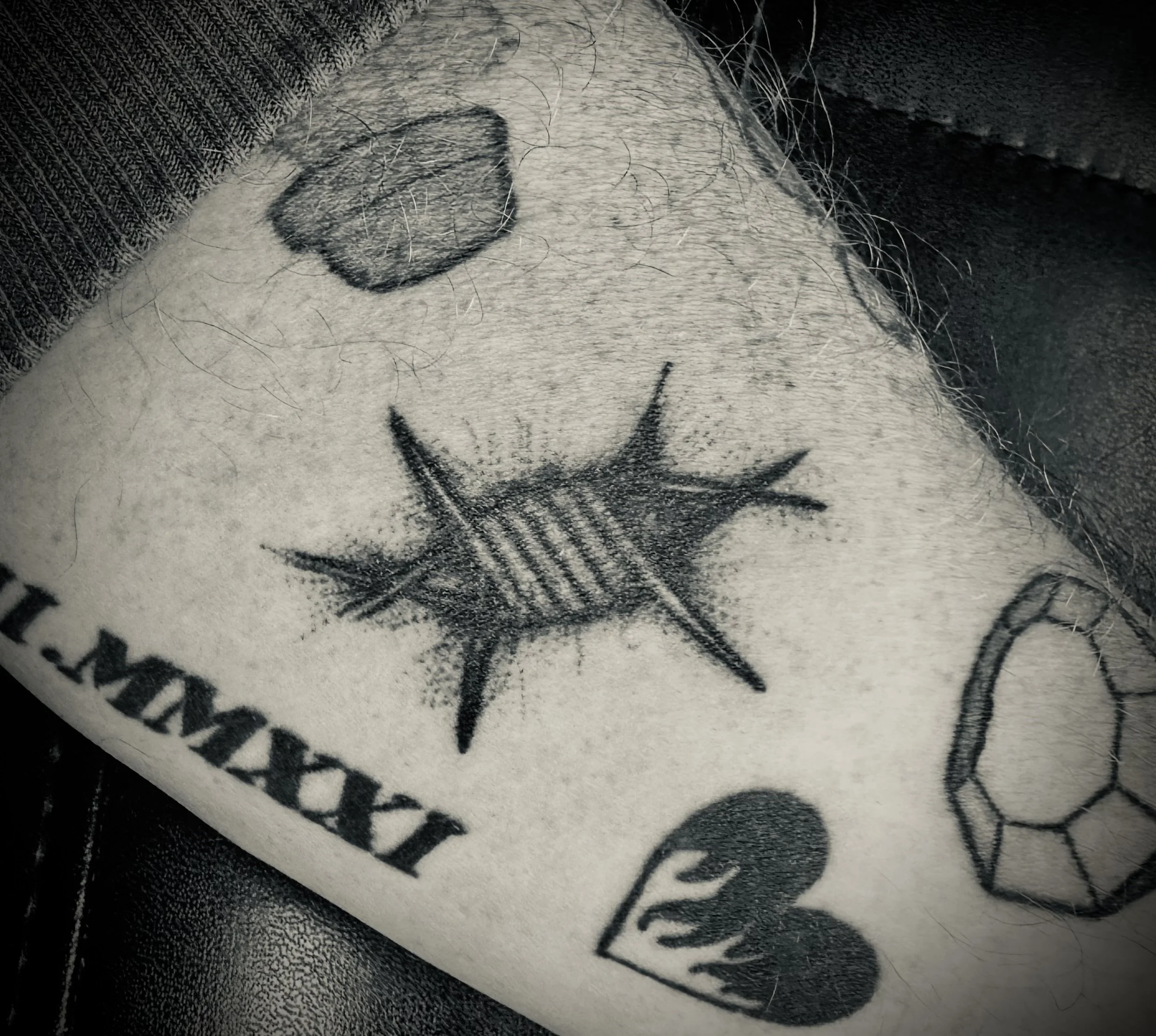 Schwarze Tätowierungen auf menschlicher Haut, darunter ein Anker, ein Herz, ein Diamant, und eine Sonne.