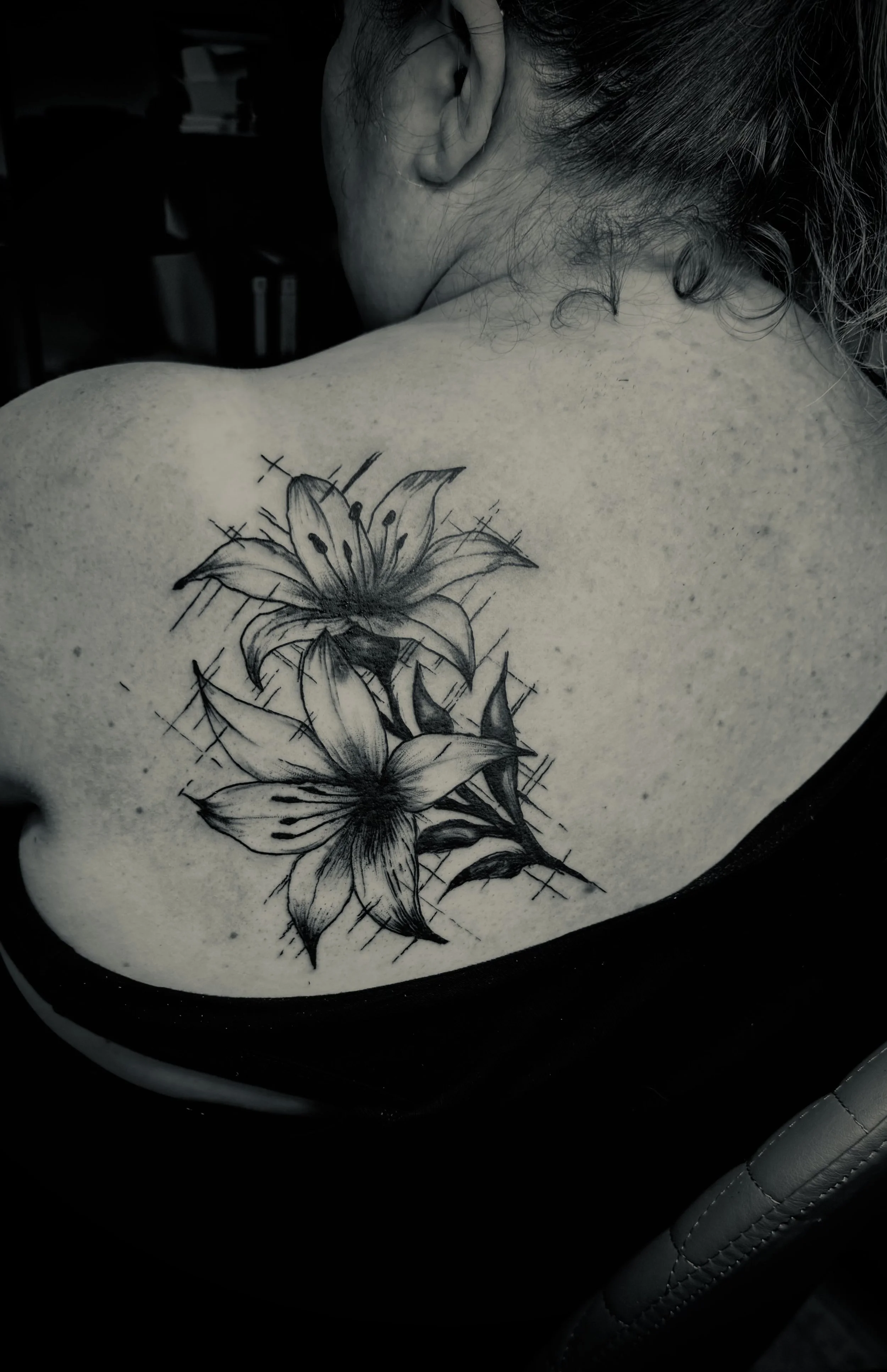 Schwarze Tätowierung von Lilien auf der Schulter einer Person.