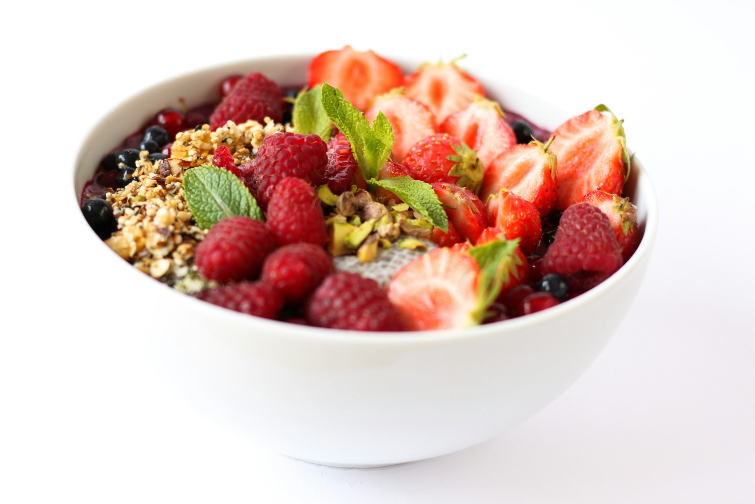 A white bowl filled with mixed berries, sliced strawberries, raspberries, blueberries, and garnished with fresh mint leaves.