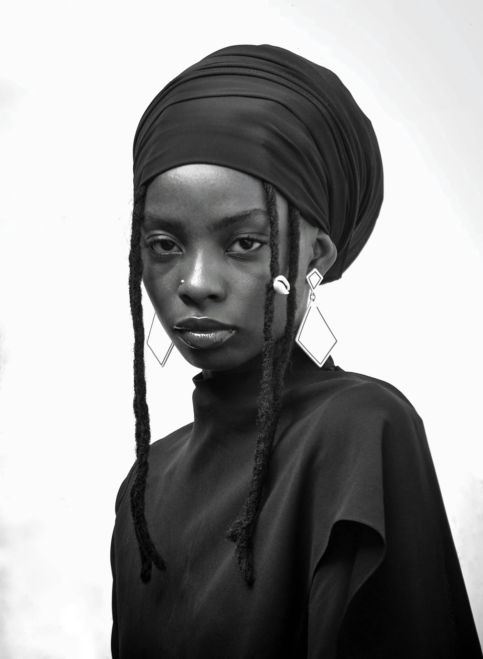 Black and white portrait of a woman with a shaved head and large circular earring, facing left in profile against a dark background.