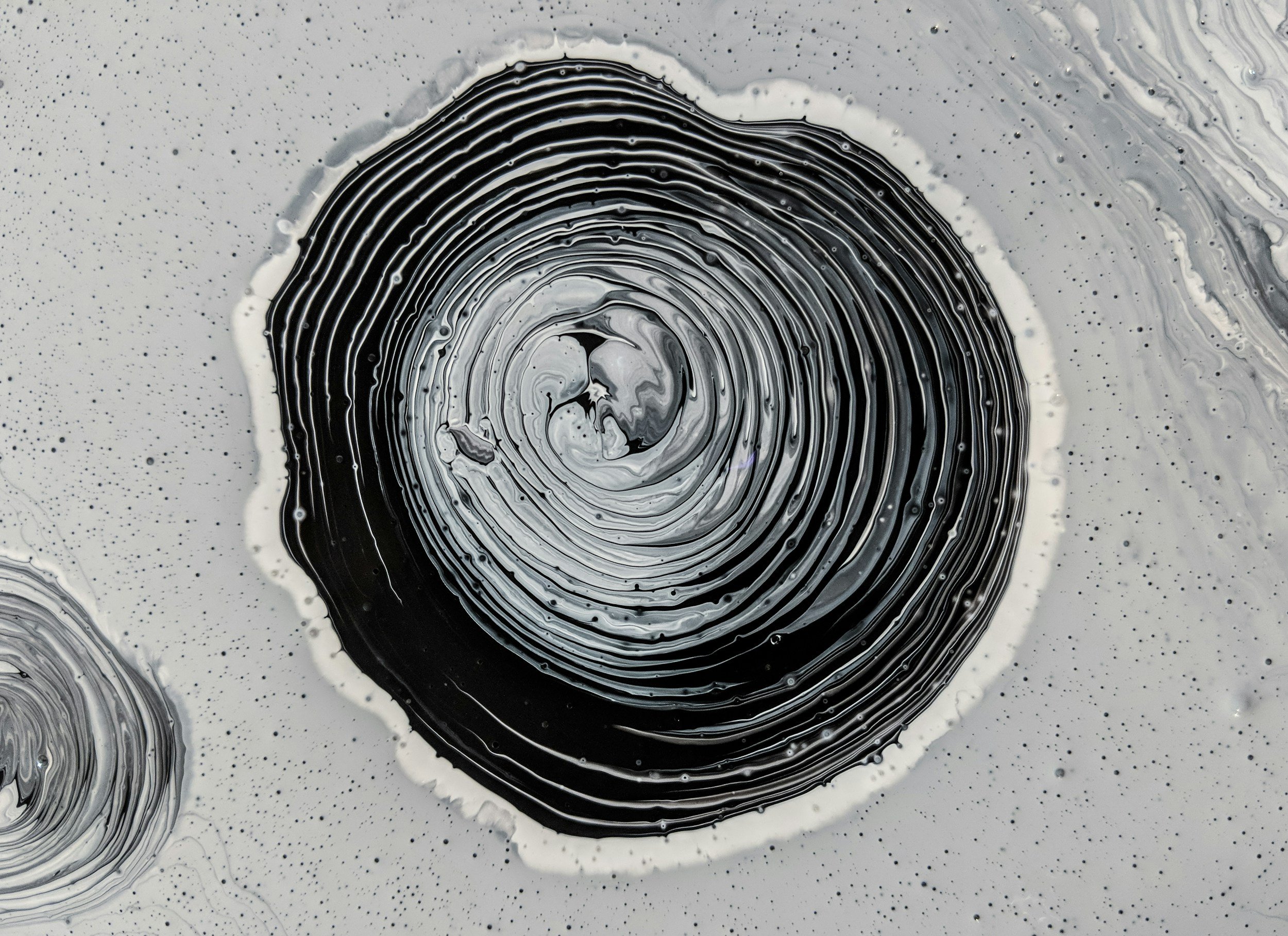 Abstract black and white swirling pattern with concentric circles and tiny dots around the central whirl.