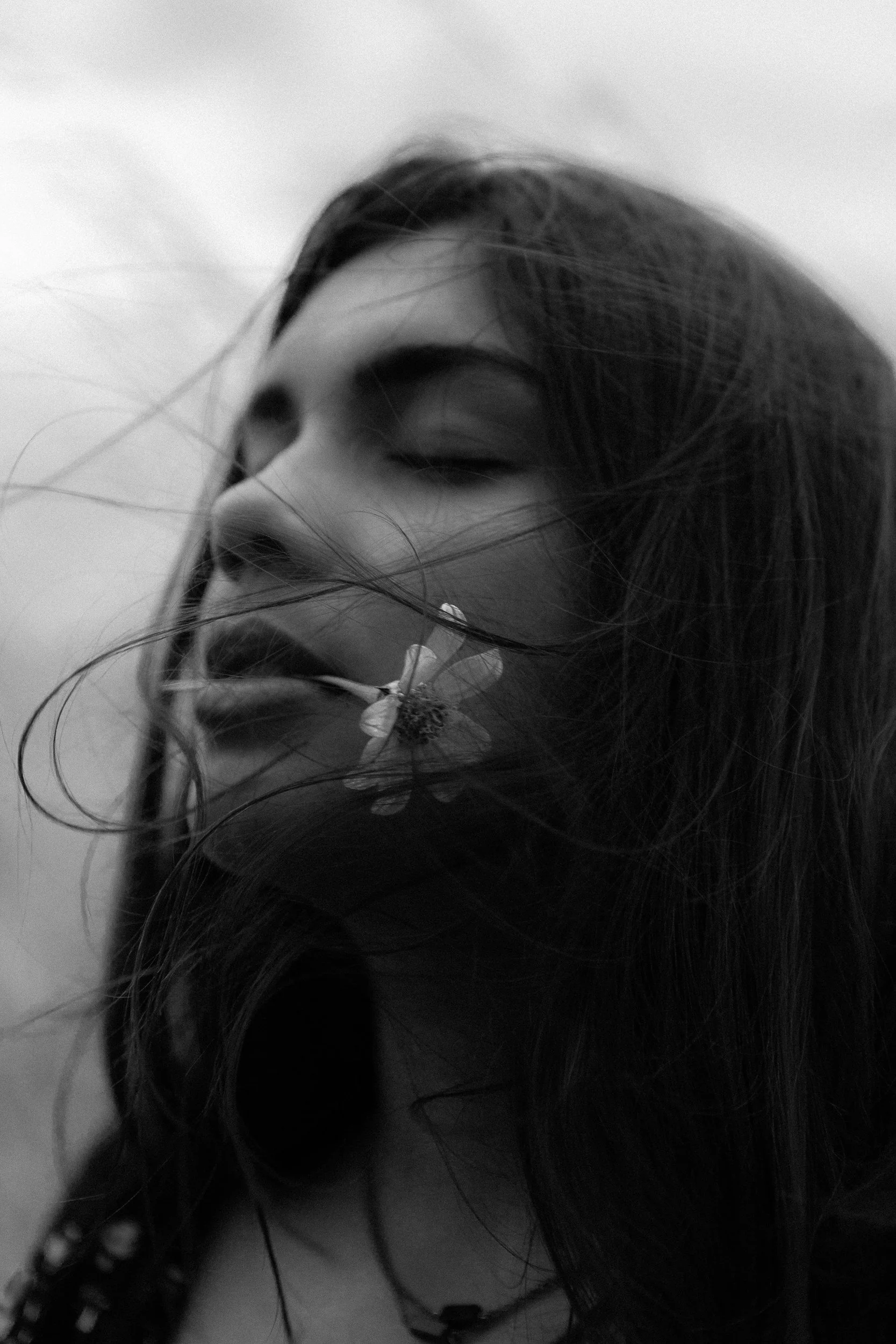 A woman with long hair holding a flower near her mouth, eyes closed, in black and white.
