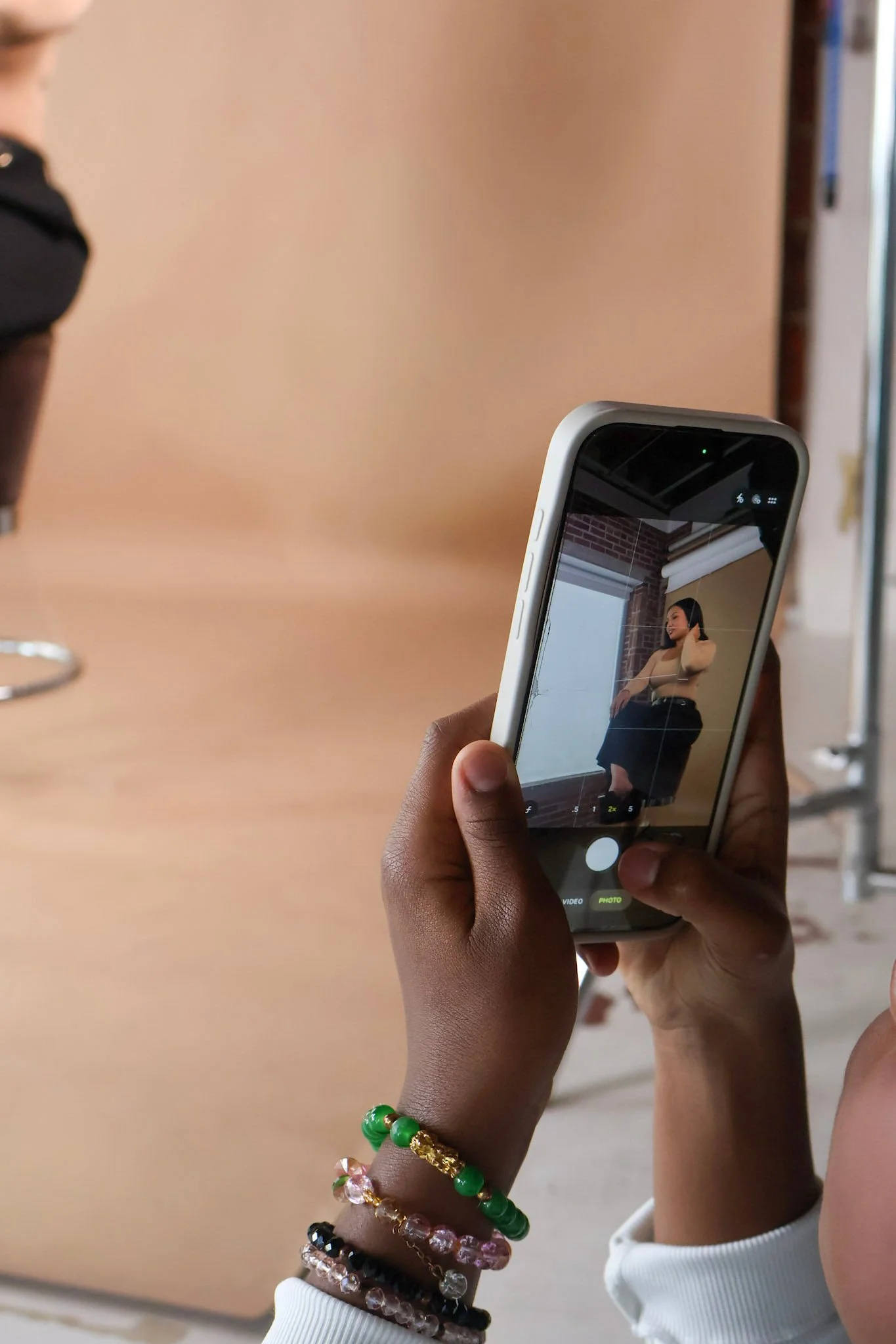 Person taking a photo of a woman seated on a chair in a studio setting.