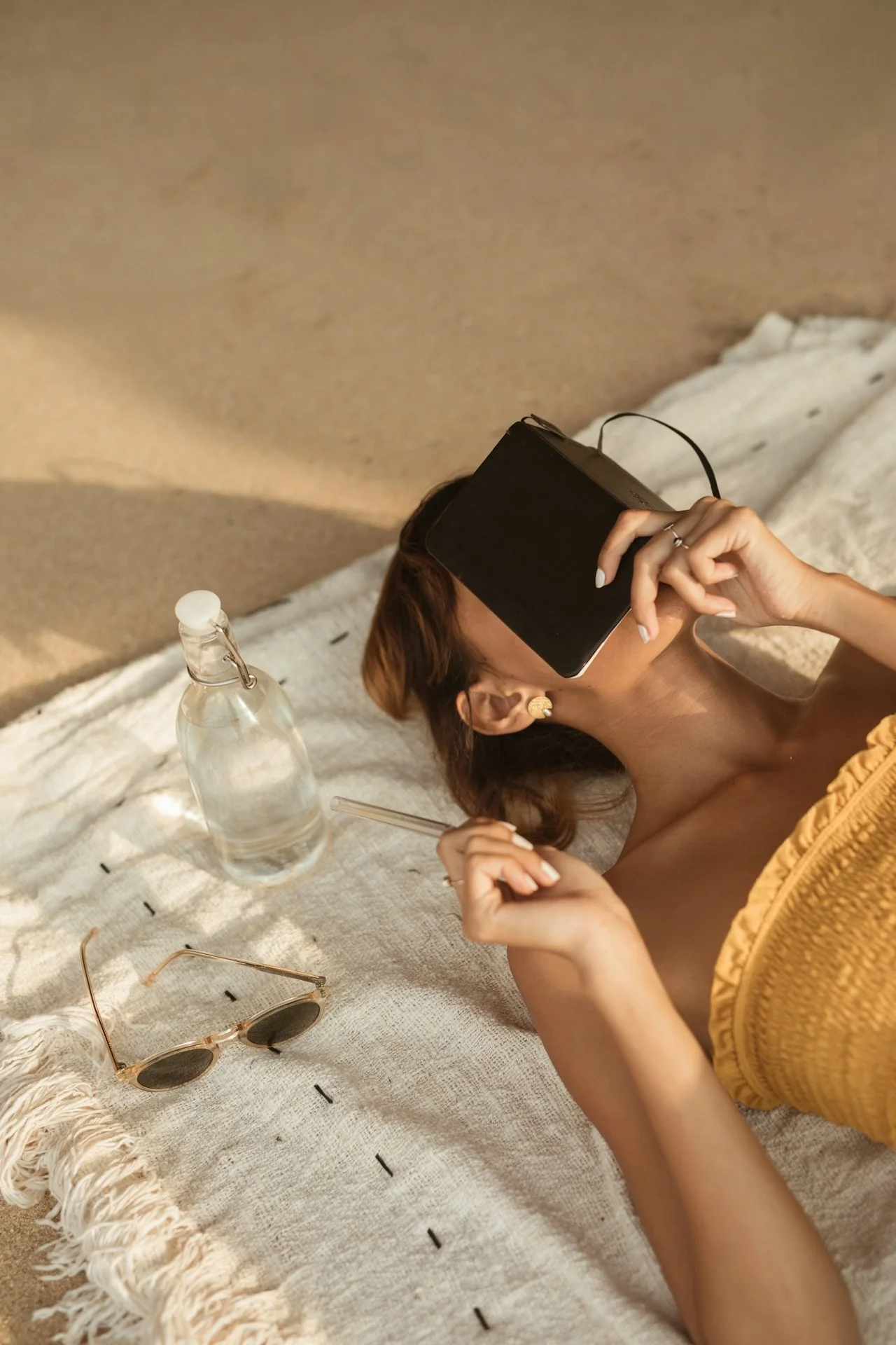 A woman lying on a rug, wearing a VR headset, holding a stylus in one hand, with sunglasses and a water bottle nearby.