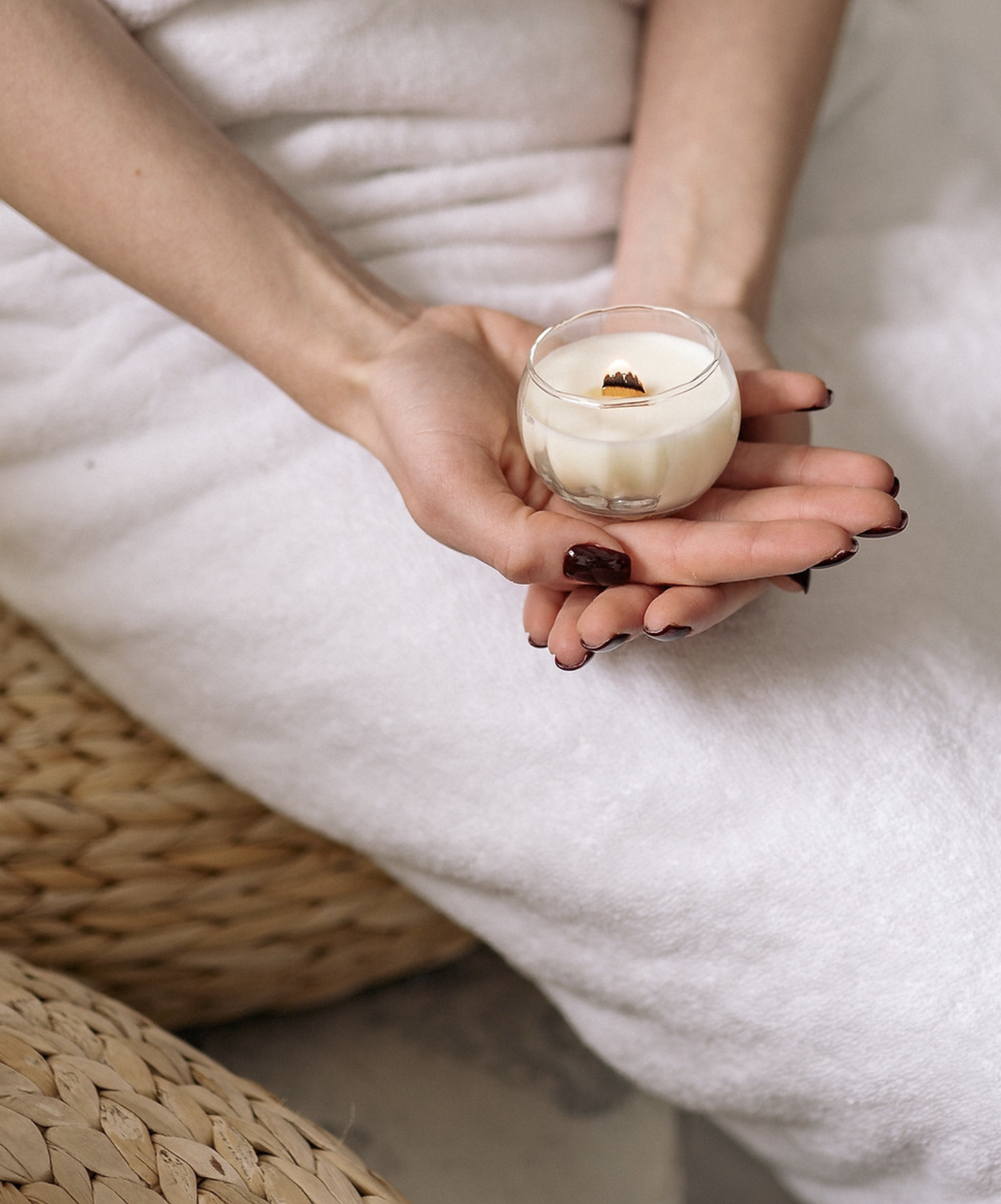 Person holding a small glass of white candle with a burning wick.