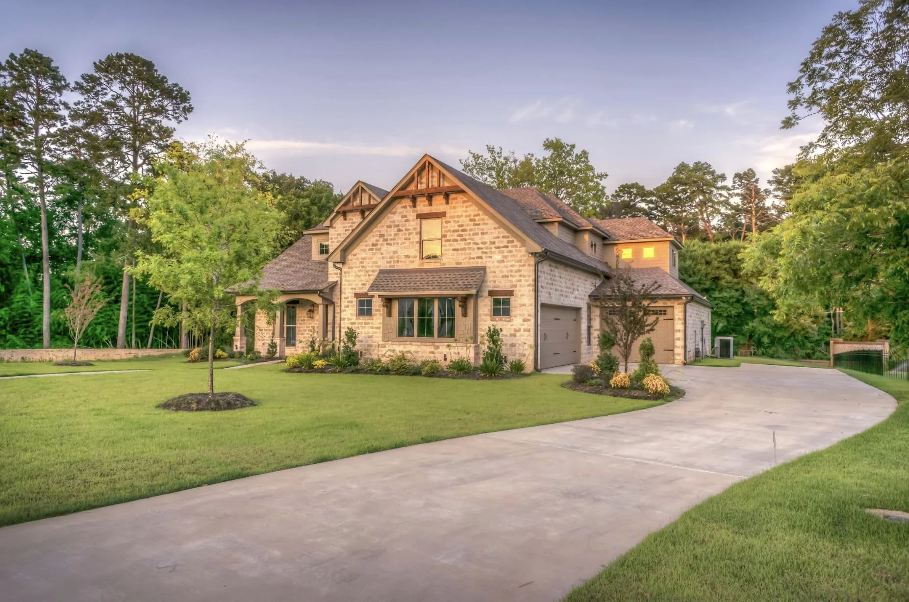 A large two-story house with stone and wood exterior, front yard with lawn and trees, and a curved concrete driveway leading to the garage.