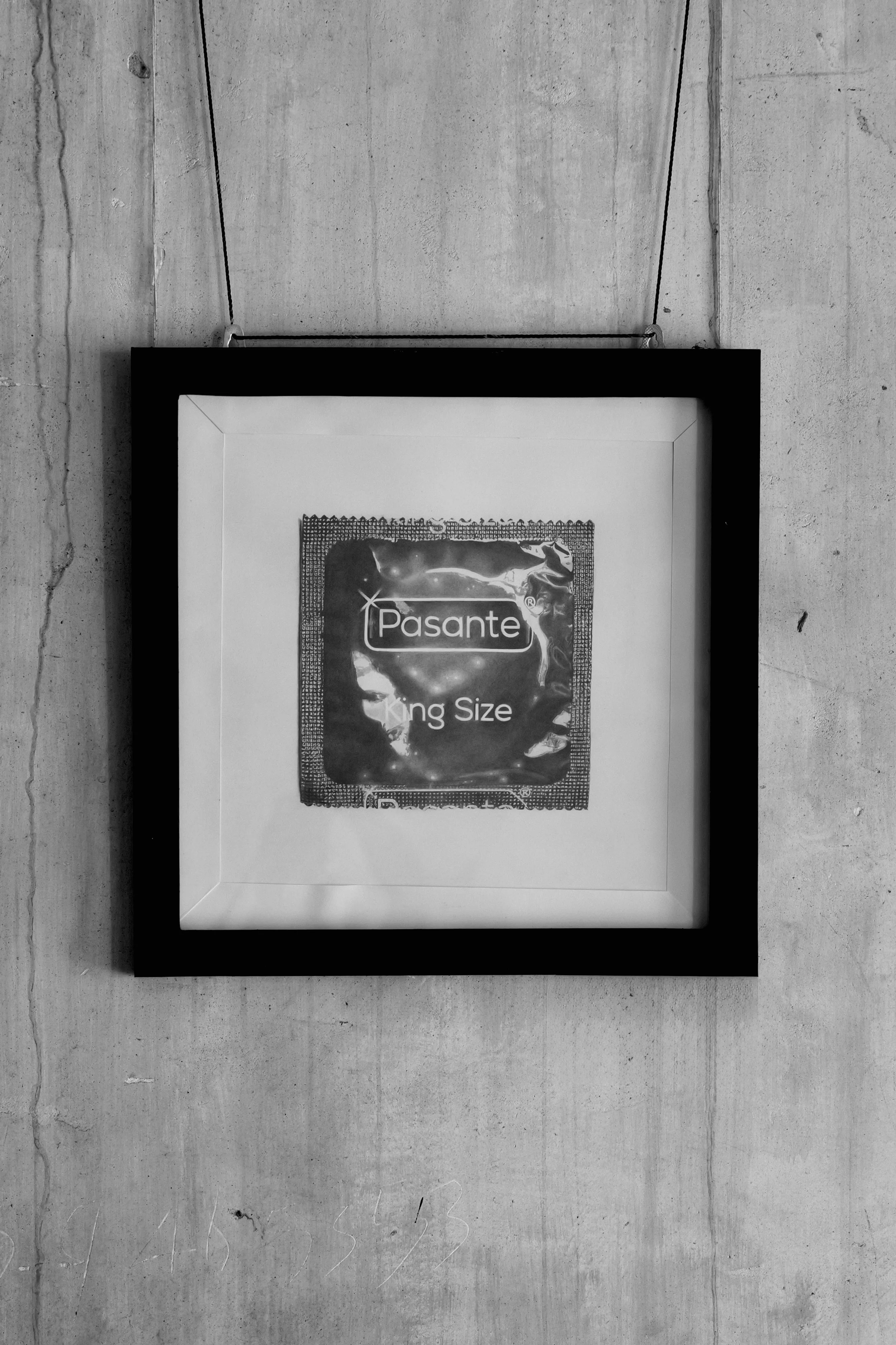 A framed poster titled 'King Size' with the word 'Pasante' on it, hanging on a concrete wall.