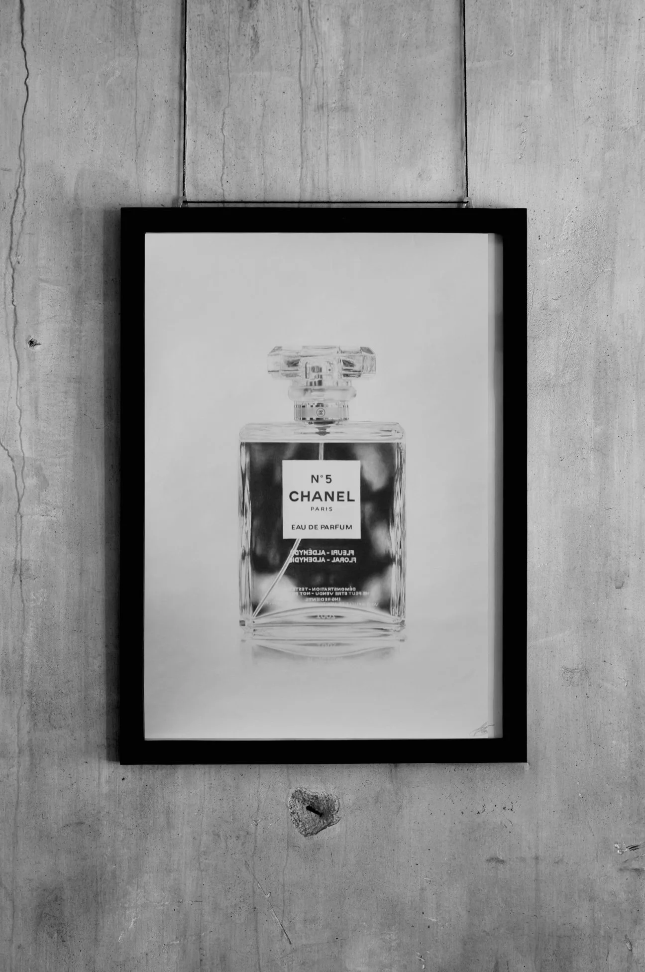 Black and white poster of a Chanel No. 5 perfume bottle with text details, hanging on a concrete wall.