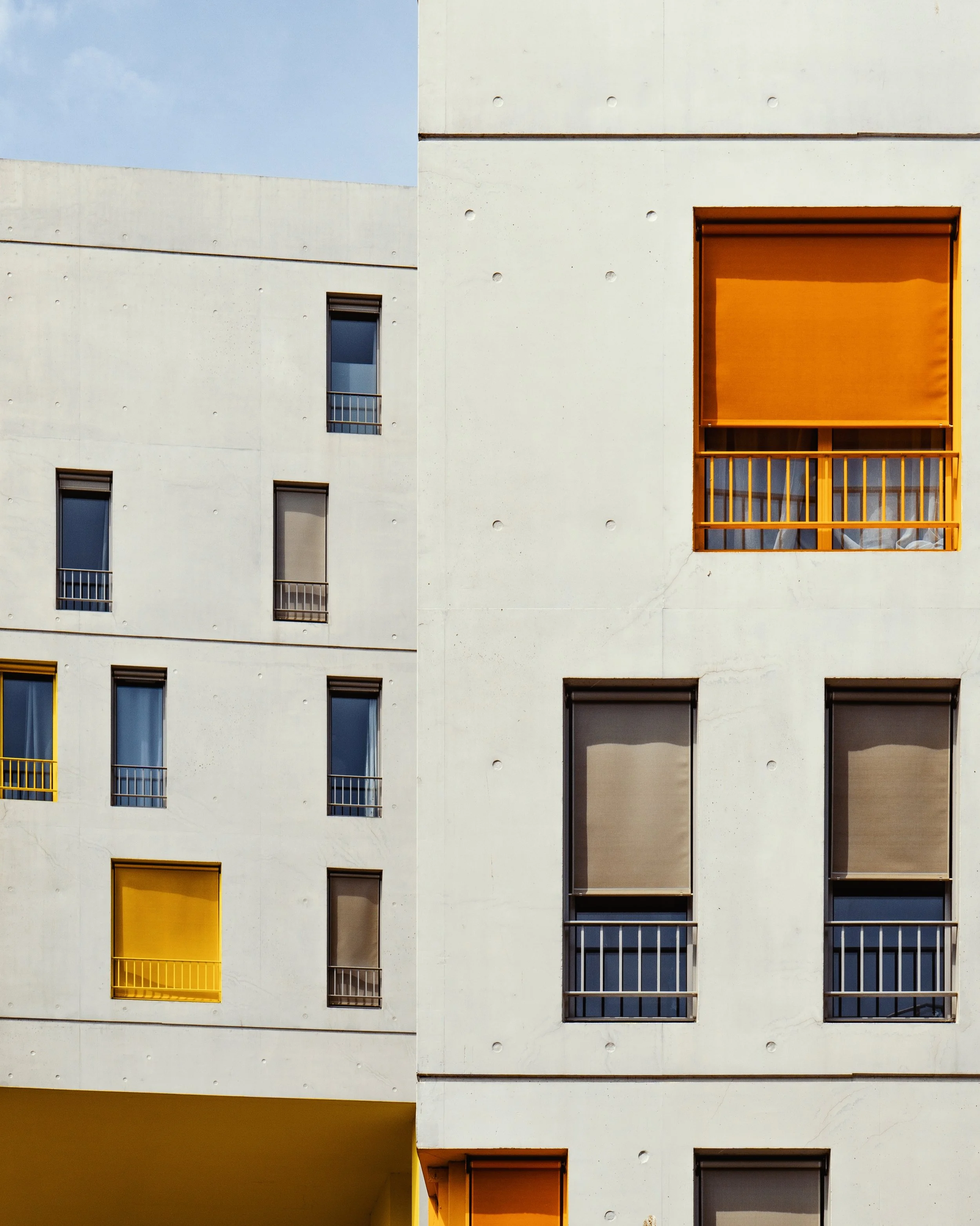 Architectural photography of modern apartment building with white walls, small rectangular windows, some with black or yellow window frames, and orange window coverings or balconies.