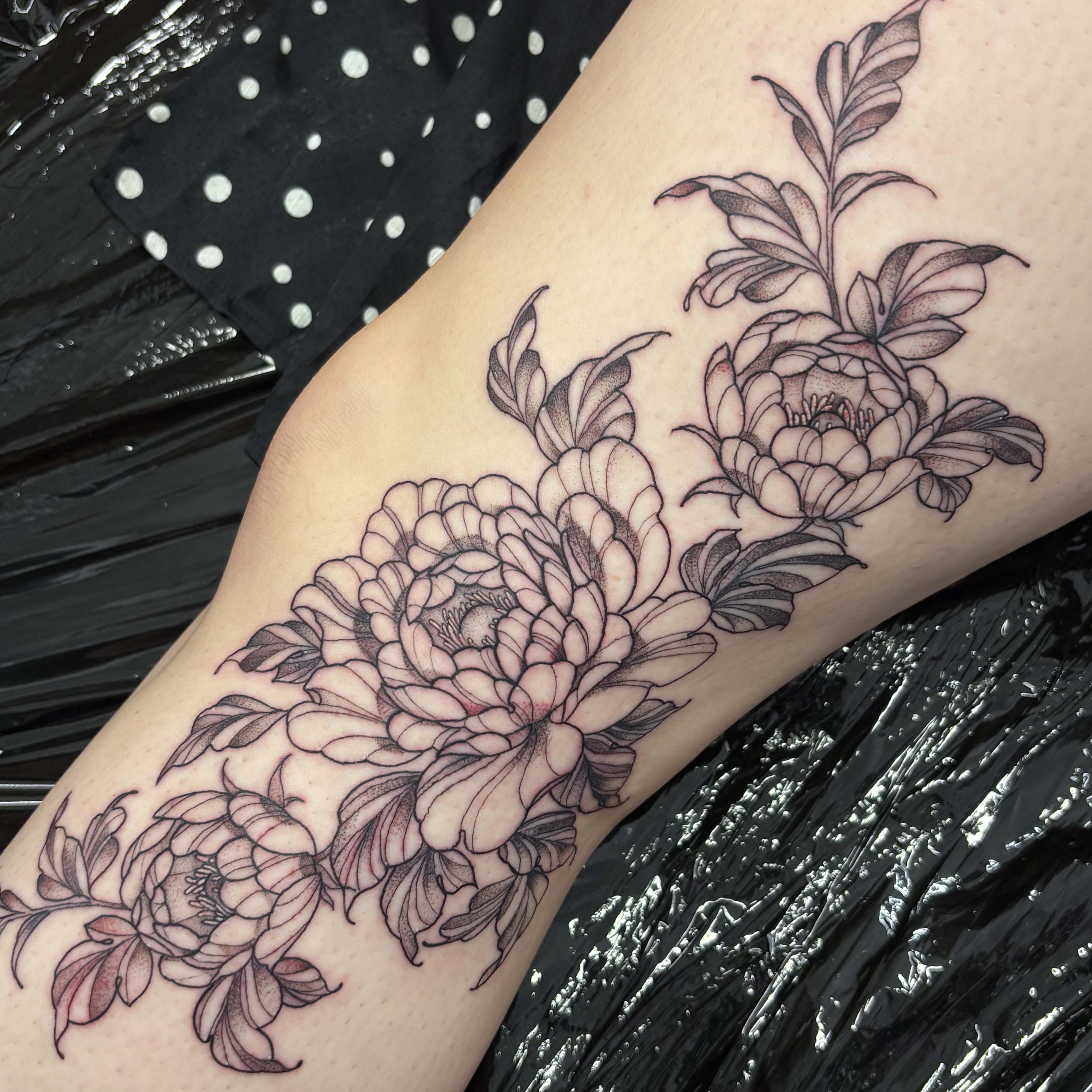 Line art tattoo of peony flowers and leaves on a person's forearm.