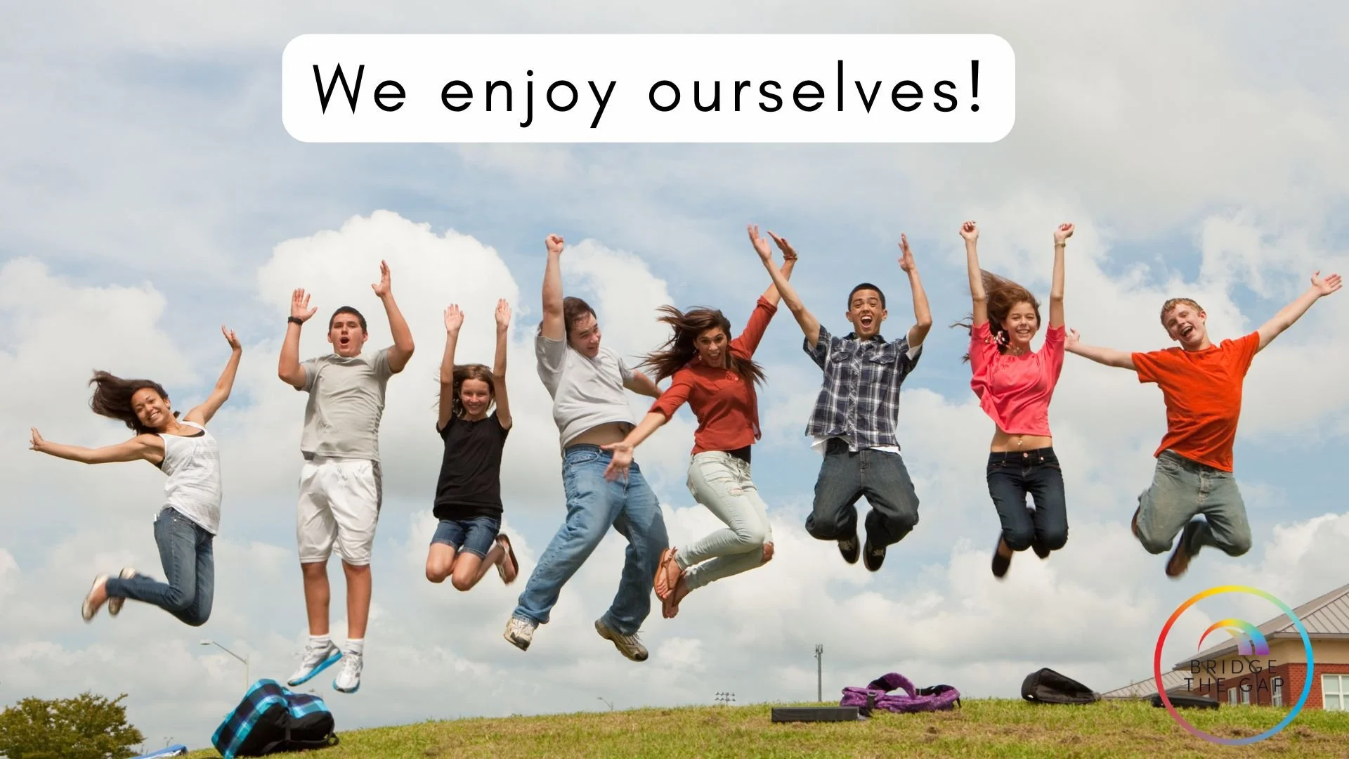 A group of nine diverse young people jumping and celebrating outdoors on a grassy hill under a partly cloudy sky, with backpacks and bags on the ground, and a logo in the bottom right corner.