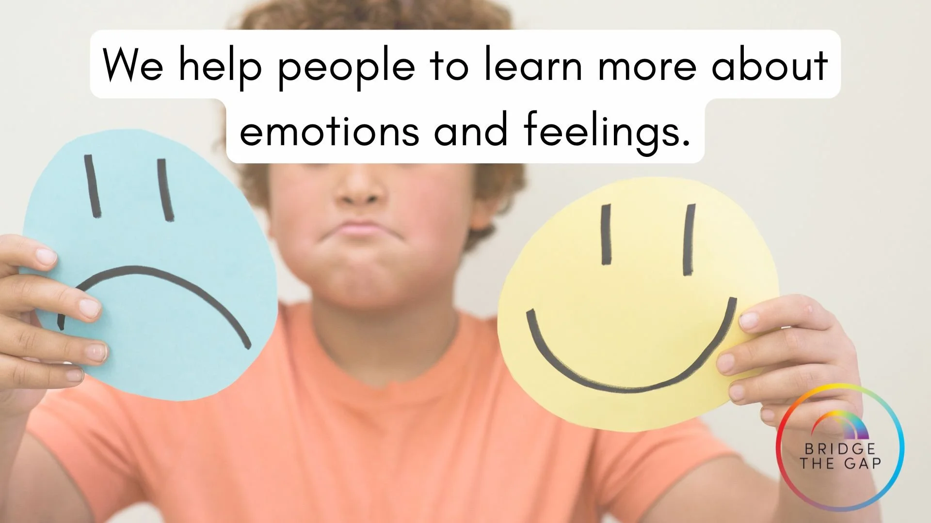 A child holding up a blue paper with a sad face and a yellow paper with a happy face, with text overlay that says 'We help people to learn more about emotions and feelings', and a logo in the bottom right corner that says 'Bridge the Gap' with a rain