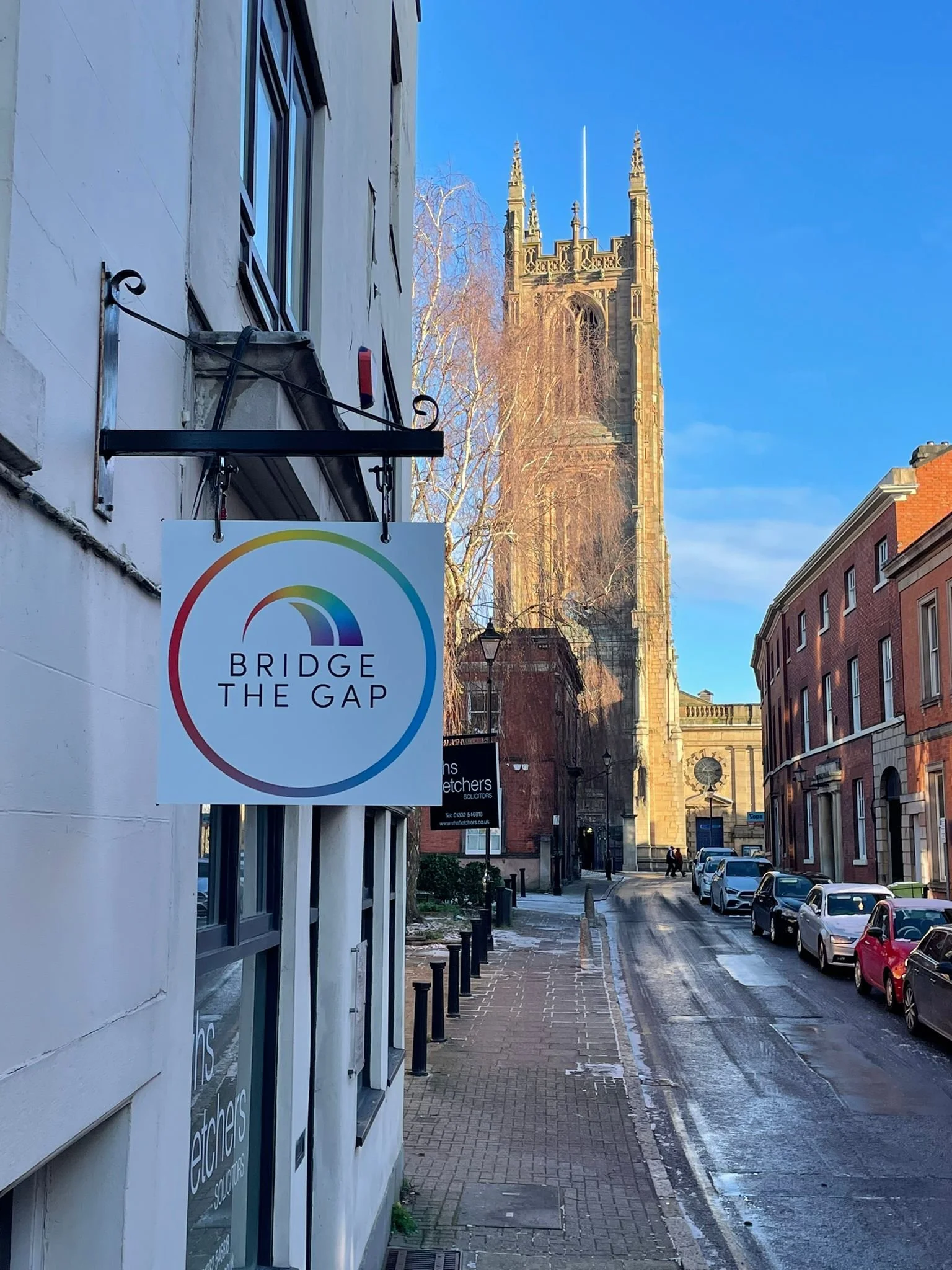 Street view with a sign that says "Bridge the Gap" and a church tower in the background.