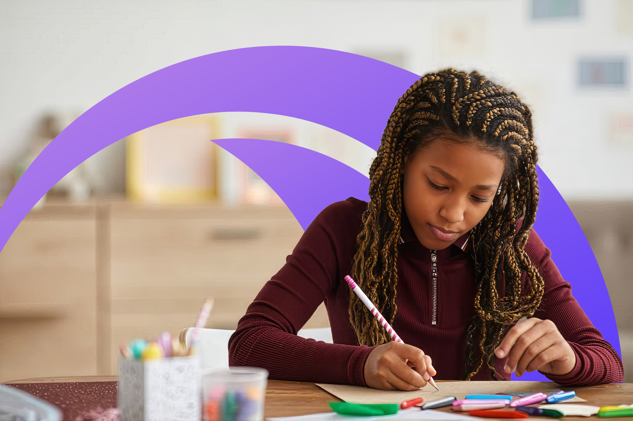 A girl with braided hair sitting at a table, writing or drawing with a pink-striped pencil on white paper. Art supplies like colorful markers, pens, and a small container of pens are on the table. The background is blurry with pastel-colored shapes and a bookshelf.