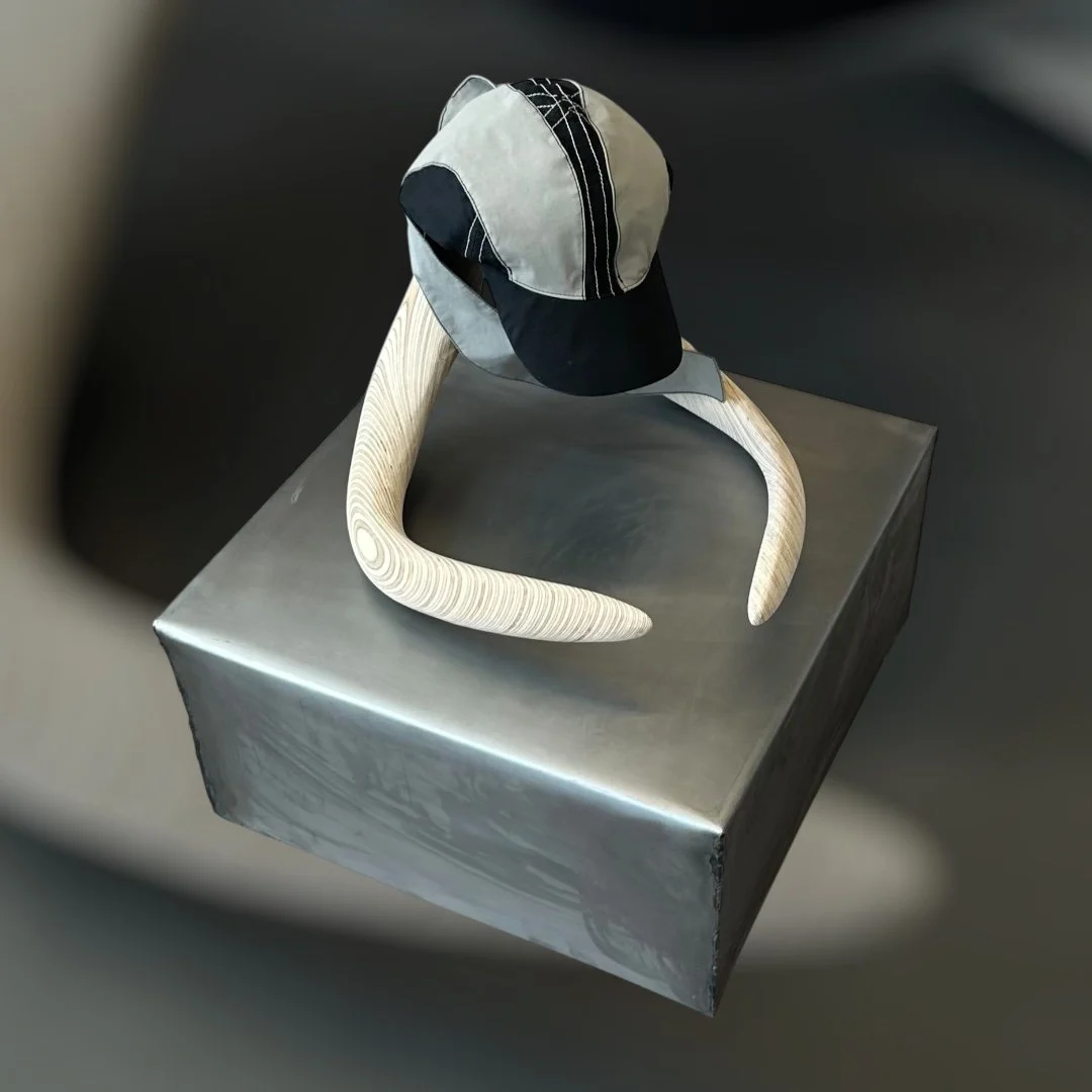 A baseball cap resting on a curved, light-colored wooden stand, positioned on a metallic silver box.