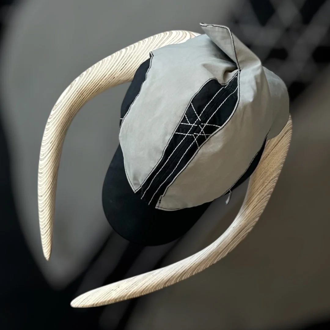 A wooden chair with rounded arms, a black head covering or cap, and a gray and black fabric bag draped over the backrest.