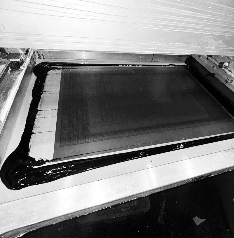 Close-up of a 3D printer bed with black adhesive or binding material around the edges, and a grid pattern on the surface.