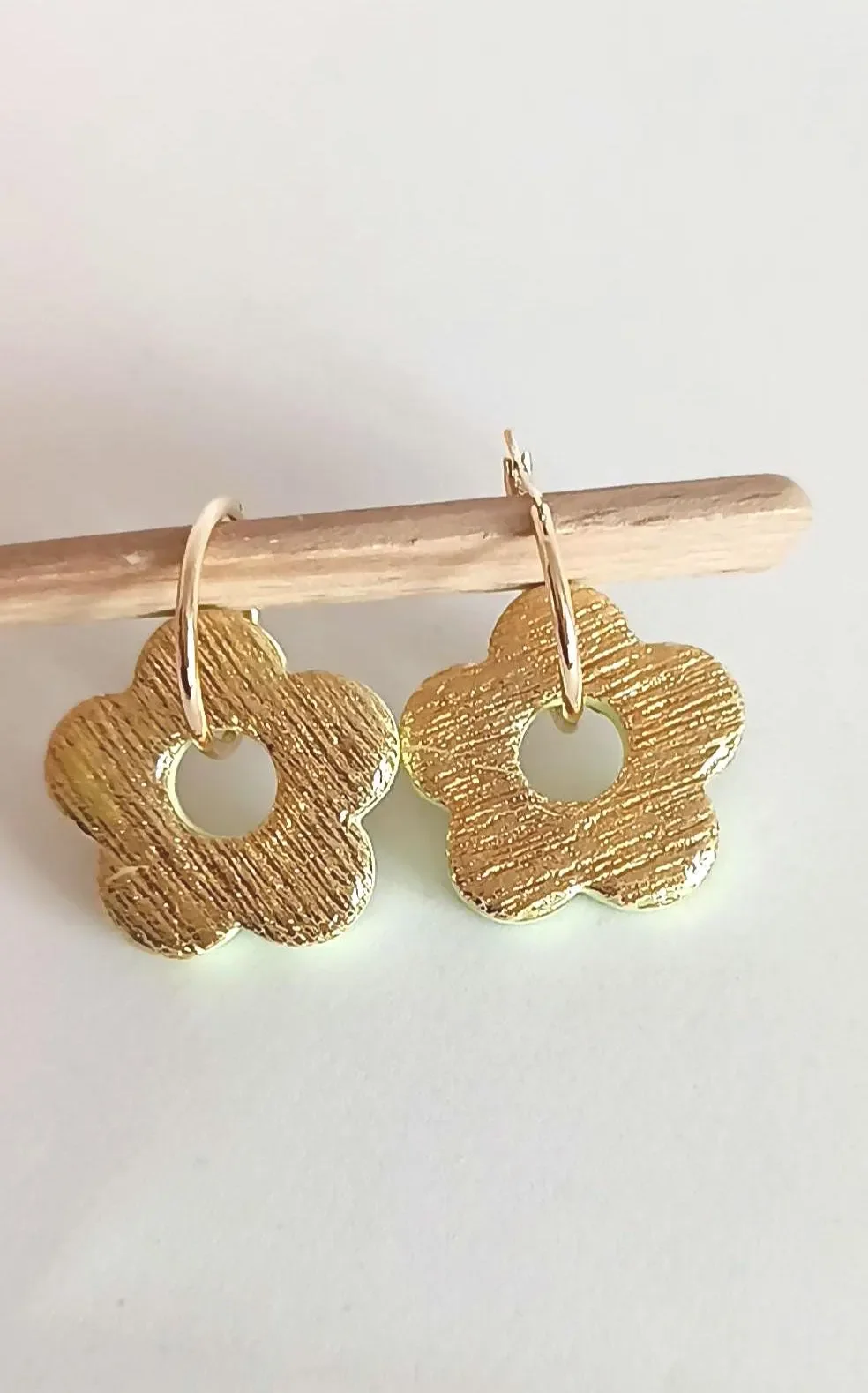 Gold hoop earrings featuring textured polymer clay flower charms. The handmade botanical dangles have a detailed surface design and hang from interchangeable gold hardware.