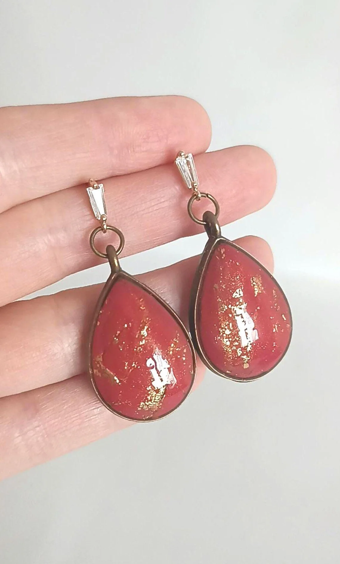 Close-up of handmade red polymer clay dangle earrings with 14k gold-filled hooks. The geometric red charms hang from tarnish-resistant gold hardware, displayed on a white background.