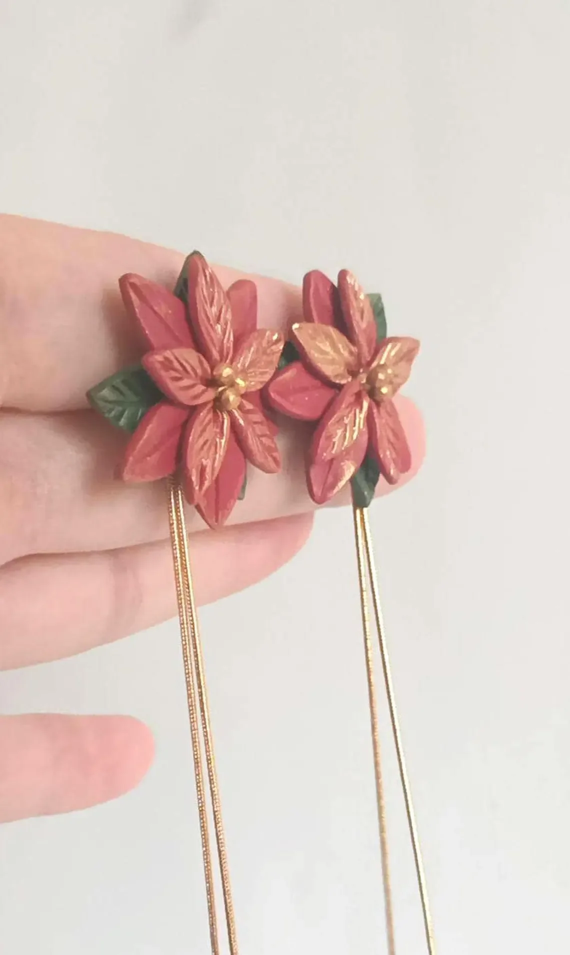 Festive red poinsettia stud earrings sculpted from polymer clay. The handmade floral studs feature green leaf details and stainless steel posts, displayed on a white background.