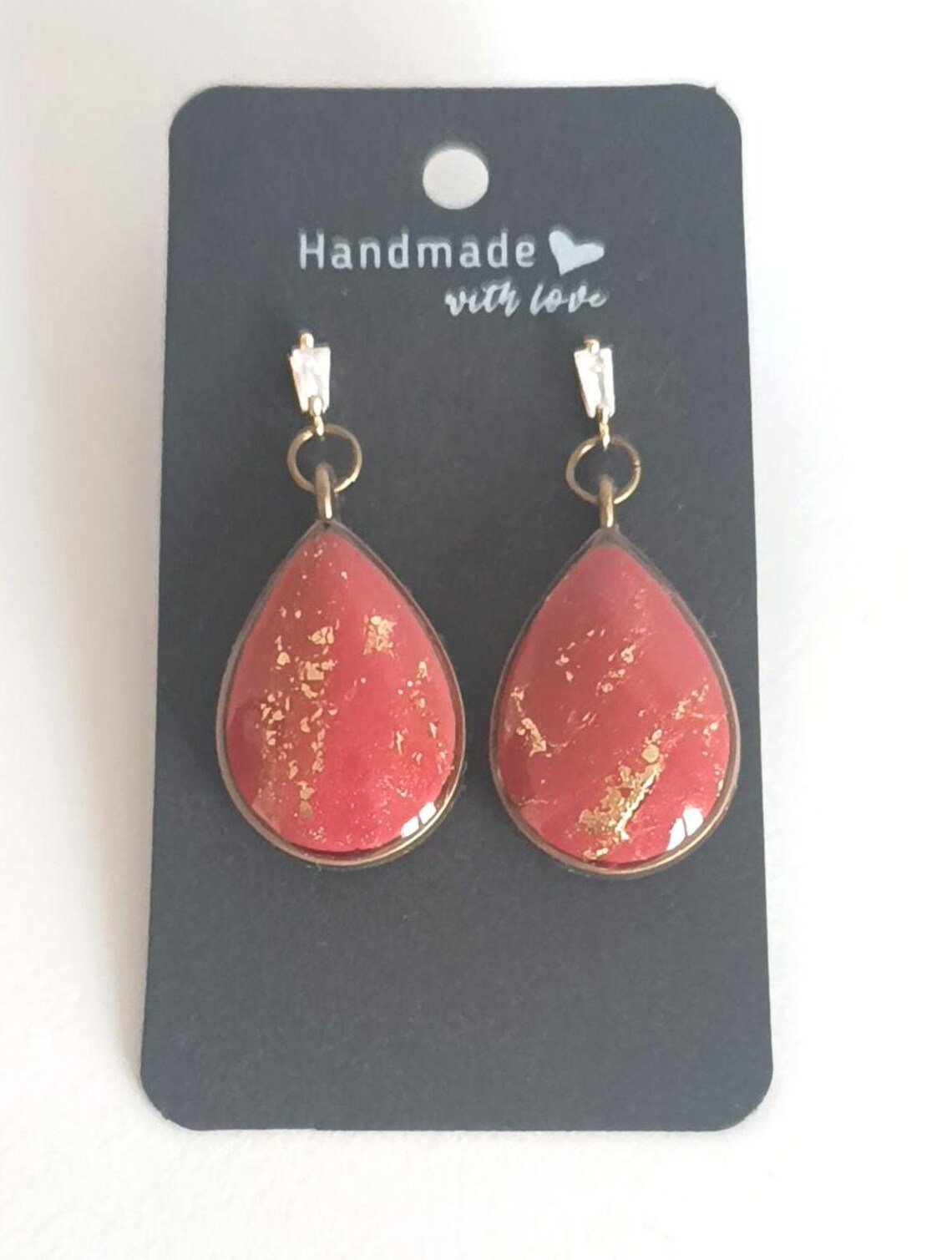 Close-up of handmade red polymer clay dangle earrings with 14k gold-filled hooks. The geometric red charms hang from tarnish-resistant gold hardware, displayed on a white background.