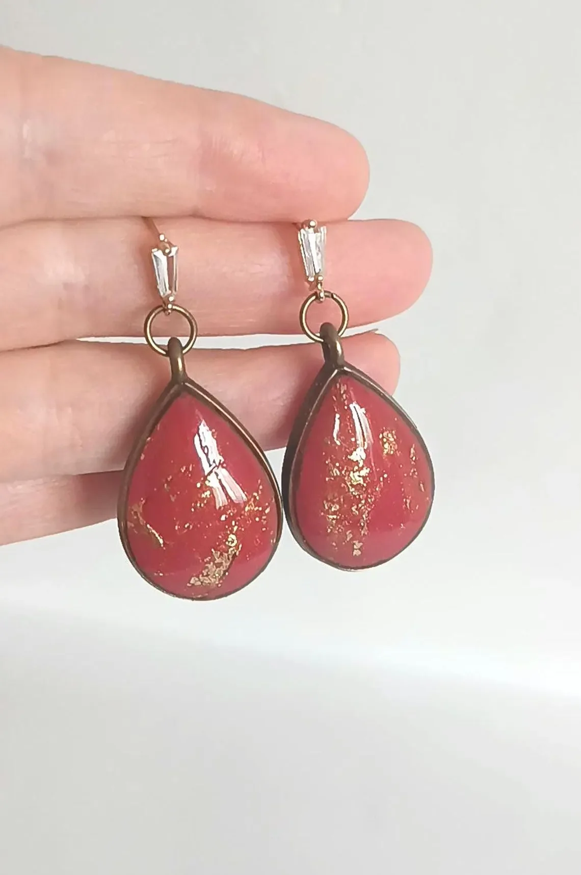 Close-up of handmade red polymer clay dangle earrings with 14k gold-filled hooks. The geometric red charms hang from tarnish-resistant gold hardware, displayed on a white background.