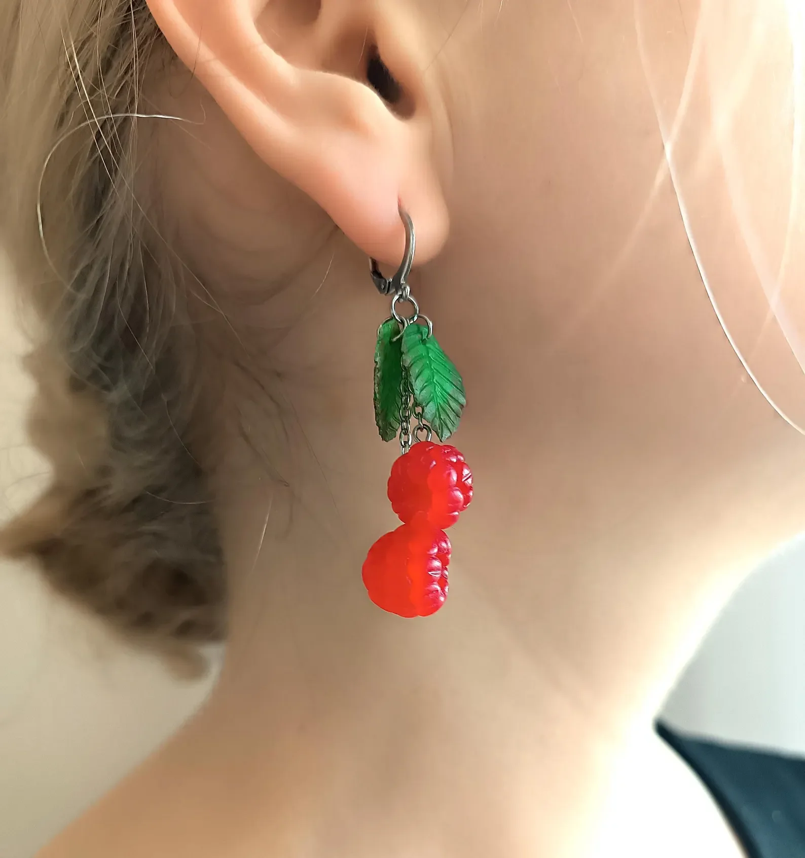 On-ear view of red polymer clay cherry earrings. Showing the lightweight size and fit of handmade fruit dangle jewelry.
