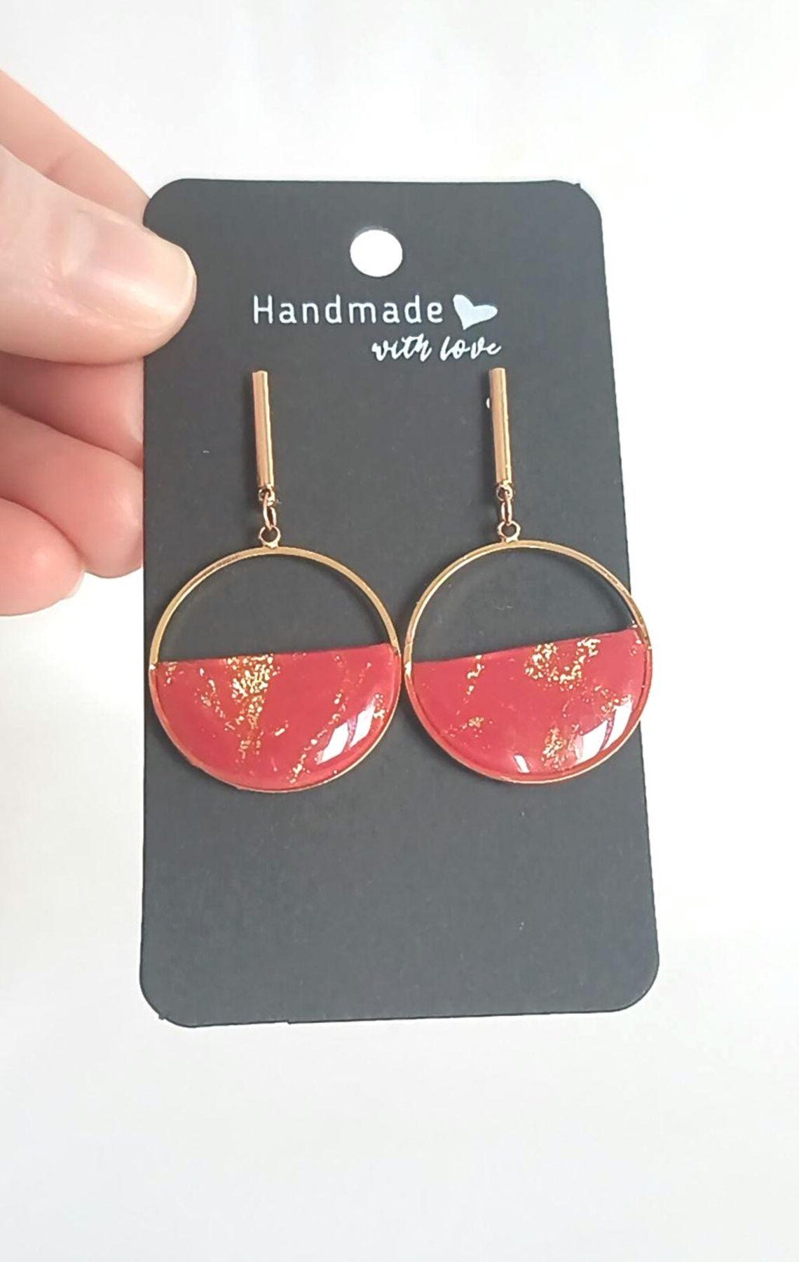 Minimalist red polymer clay circle earrings hanging from 14k gold-filled hooks. The round geometric dangles feature a matte red finish and are displayed on a white background.