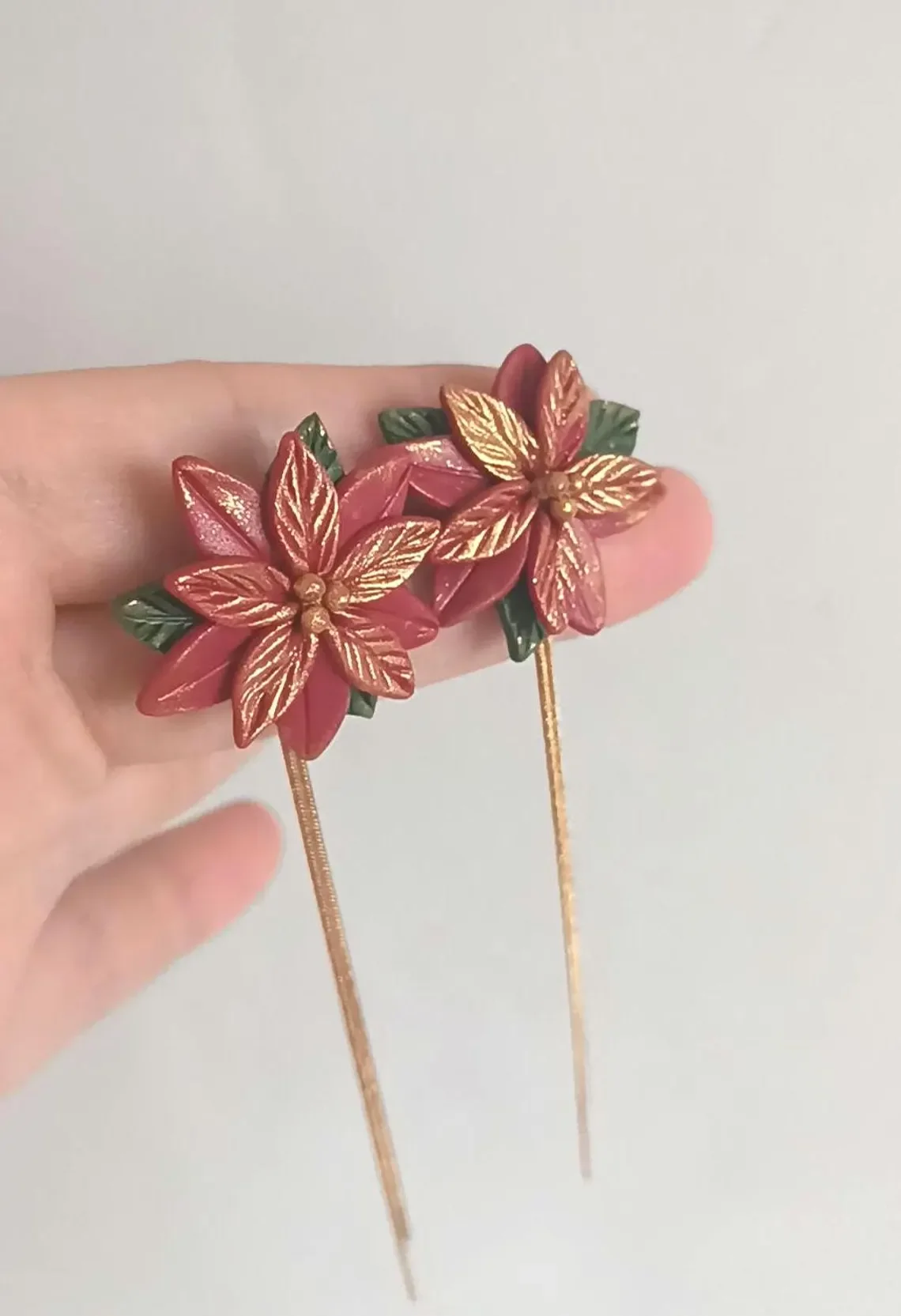 Festive red poinsettia stud earrings sculpted from polymer clay. The handmade floral studs feature green leaf details and stainless steel posts, displayed on a white background.